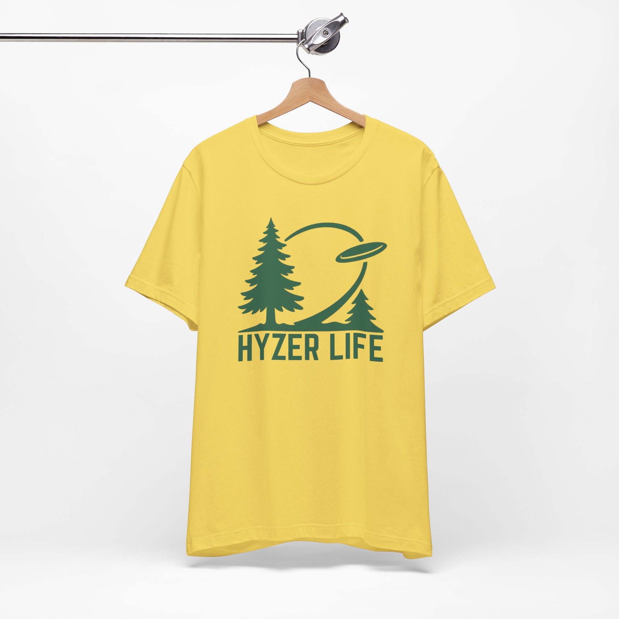 Yellow t-shirt with green graphic of trees and a disc golf flying with the words 'HYZER LIFE' below the image, on a hanger against a white backgroud