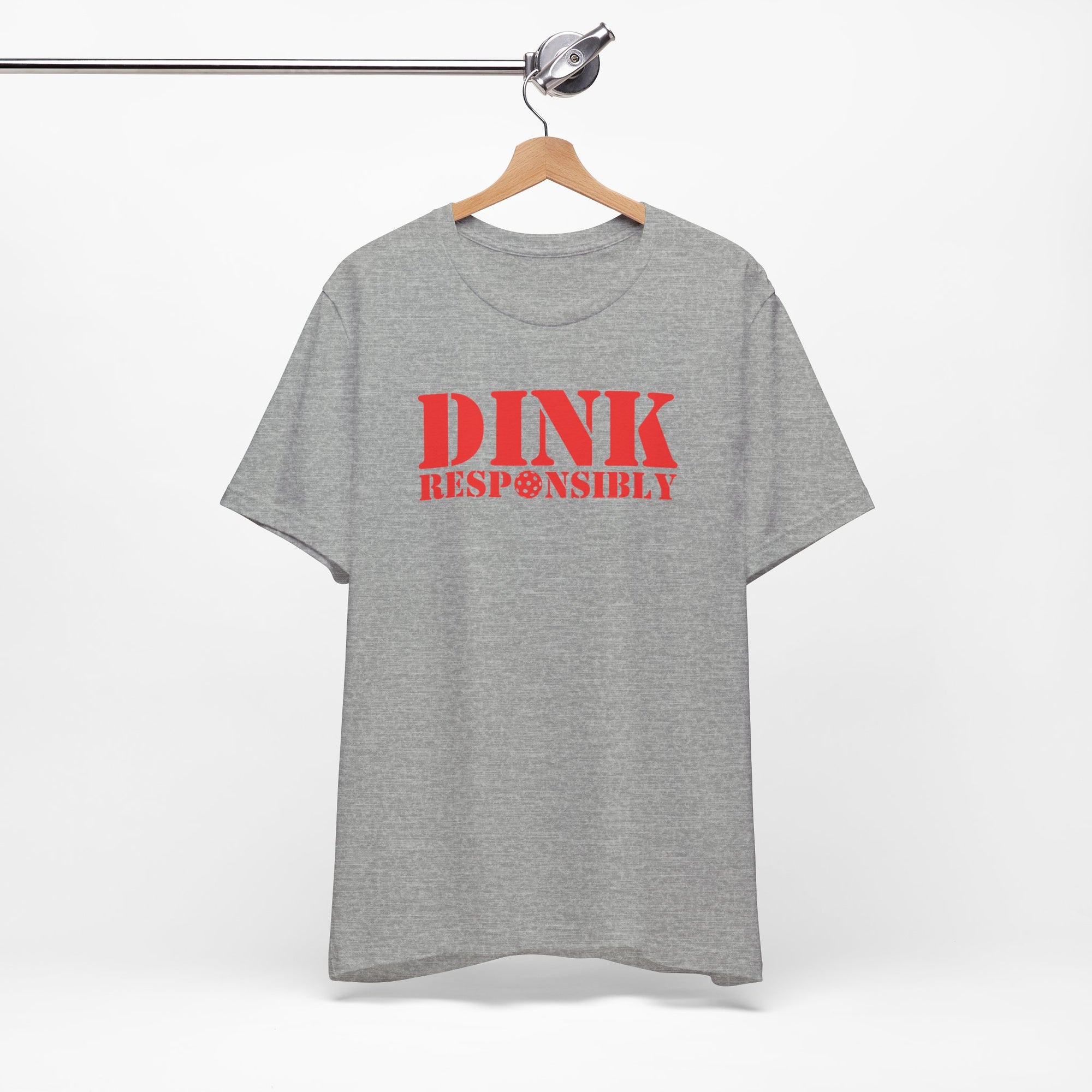 Light gray t-shirt with red text 'DINK RESPONSIBLY' with a pickleball replacing the "O" in "Responsibly" on a hanger against a white background