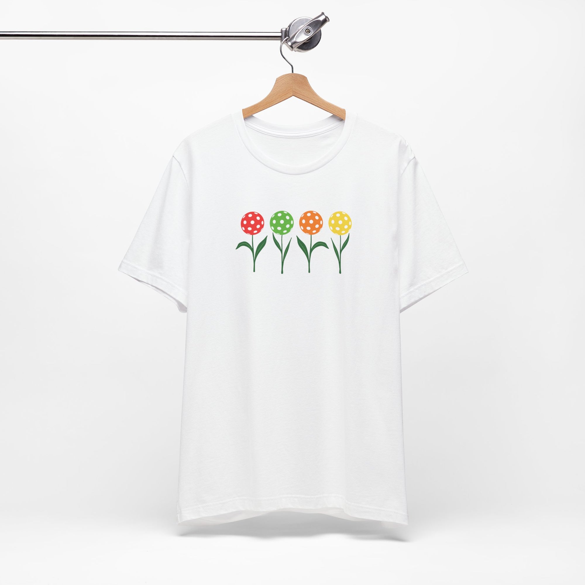 White t-shirt with colorful flowers made from pickleballs on green stems with leaves, on a hanger against a white background