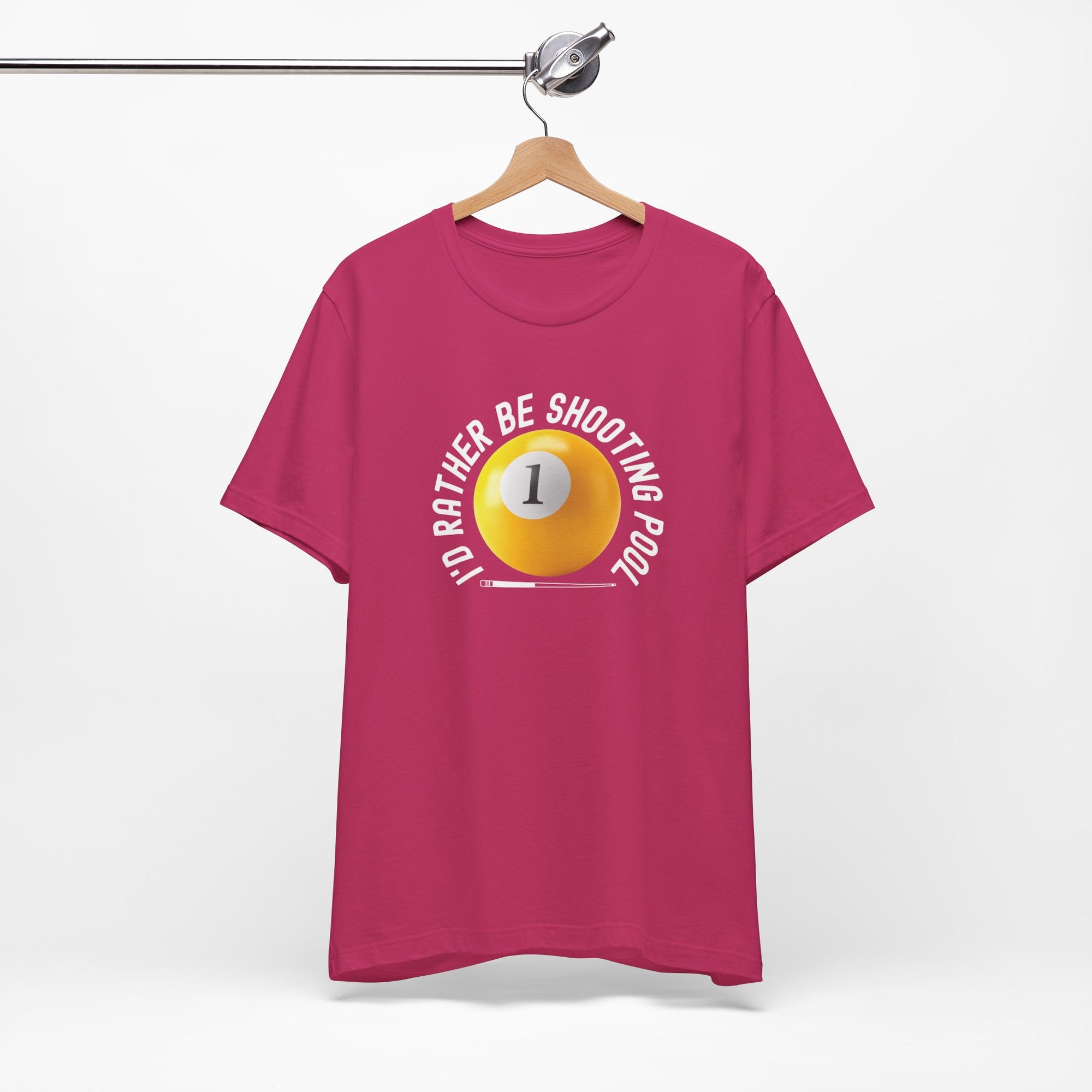 Pink t-shirt with a yellow billiards ball and cue stick graphic and the text "I'd Rather Be Shooting Pool" on a hanger against a white background