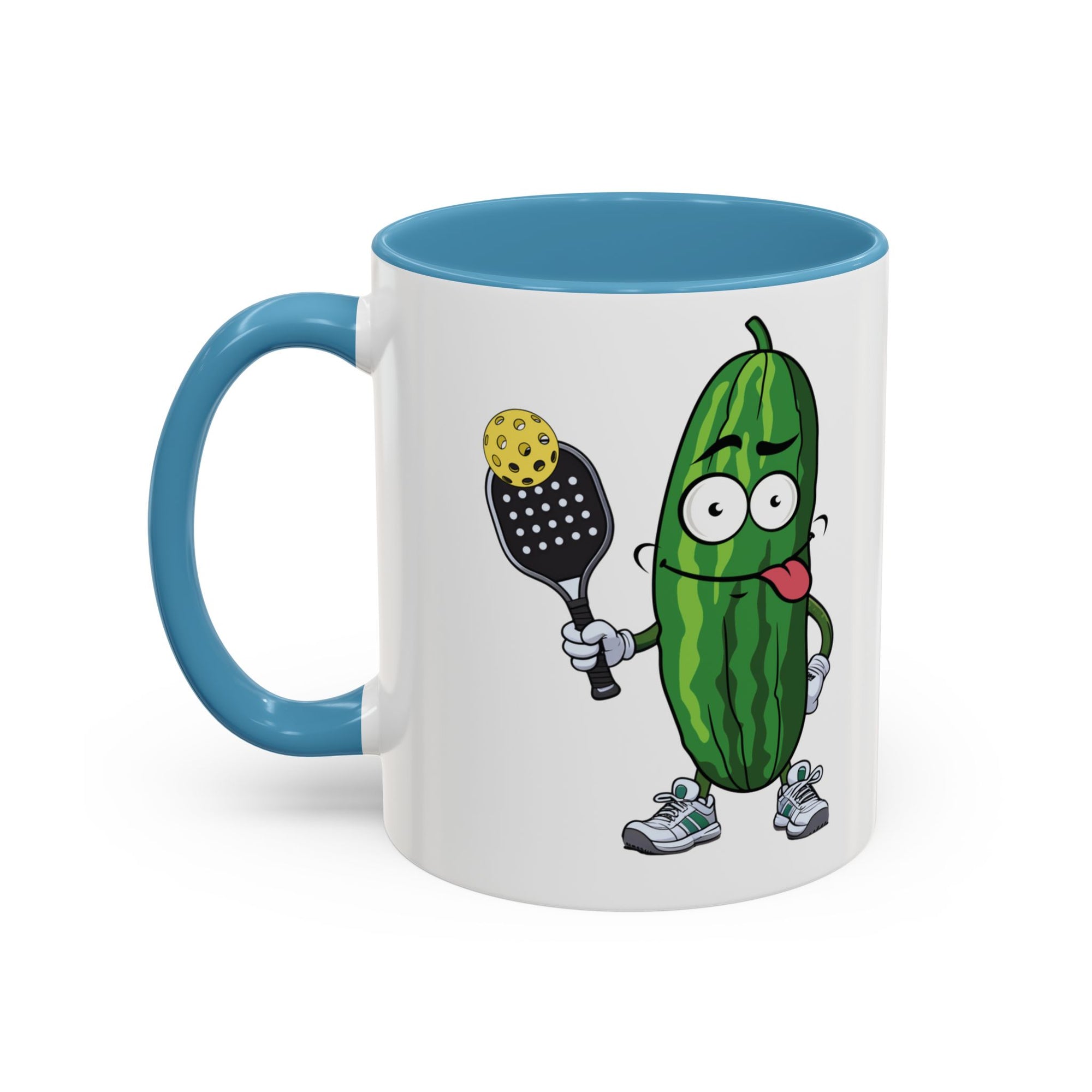 A ceramic coffee mug with light blue accents on the handle and interior, with a cartoon pickle with googly eyes and his tongue sticking out, holding a pickleball paddle with a yellow pickleball, against a white background