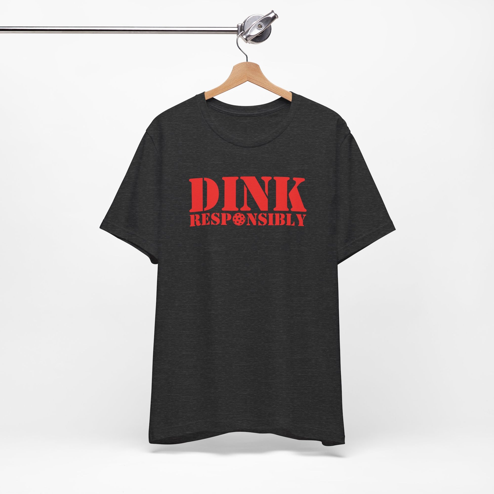 Dark gray t-shirt with red text 'DINK RESPONSIBLY' with a pickleball replacing the "O" in "Responsibly" on a hanger against a white background
