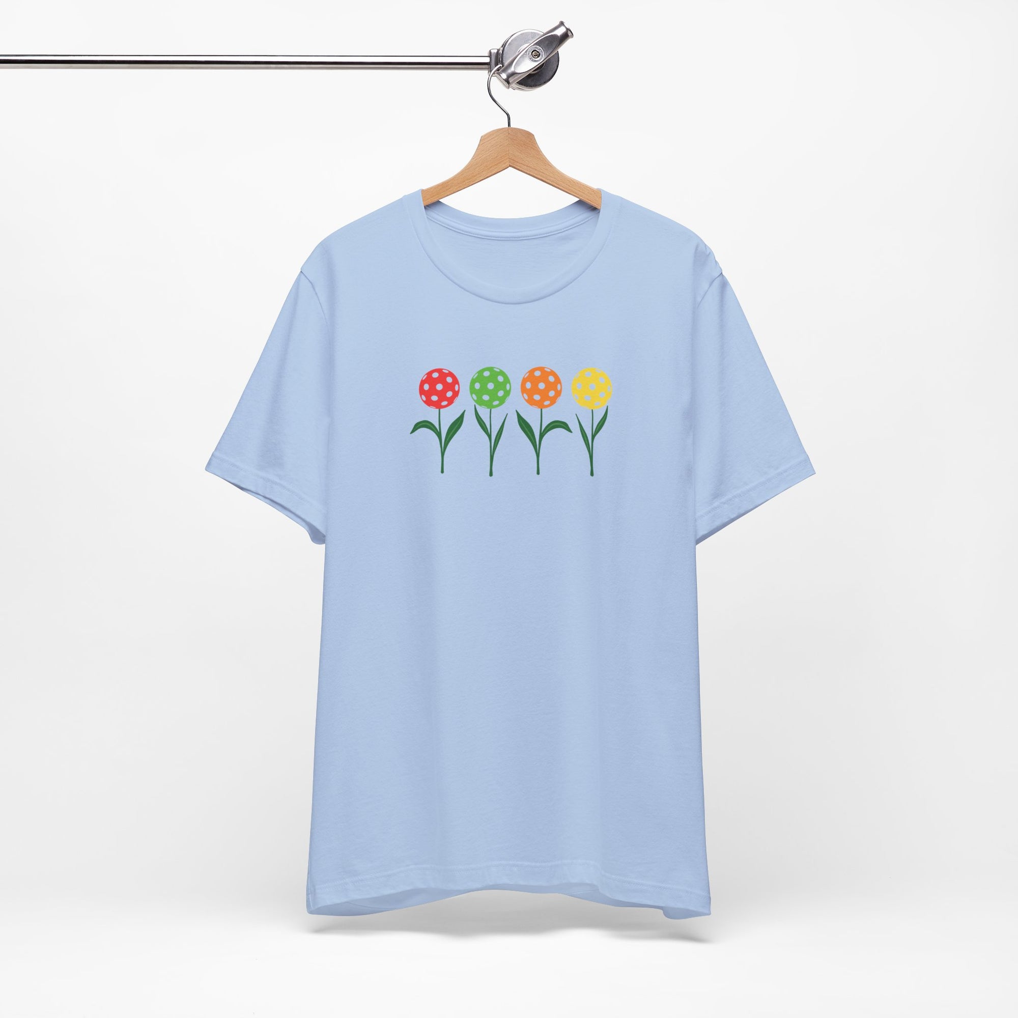 Light blue t-shirt with colorful flowers made from pickleballs on green stems with leaves, on a hanger against a white background