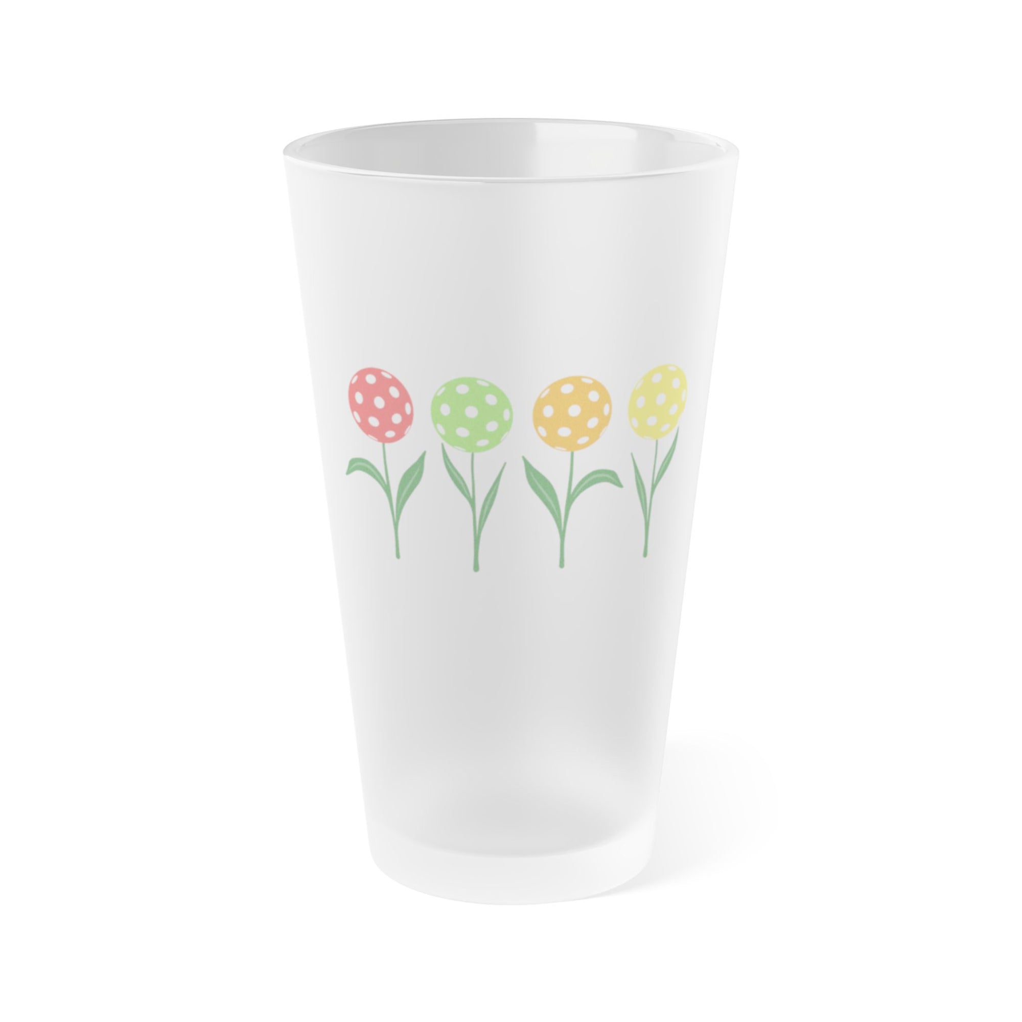A frosted pint glass with four colorful flowers made out of pickleballs, on a white background.