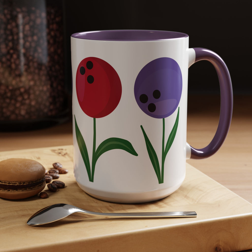A white ceramic coffee mug with purple accents on the handle and interior, with colorful flowers made out of bowling balls, in a coffee shop setting