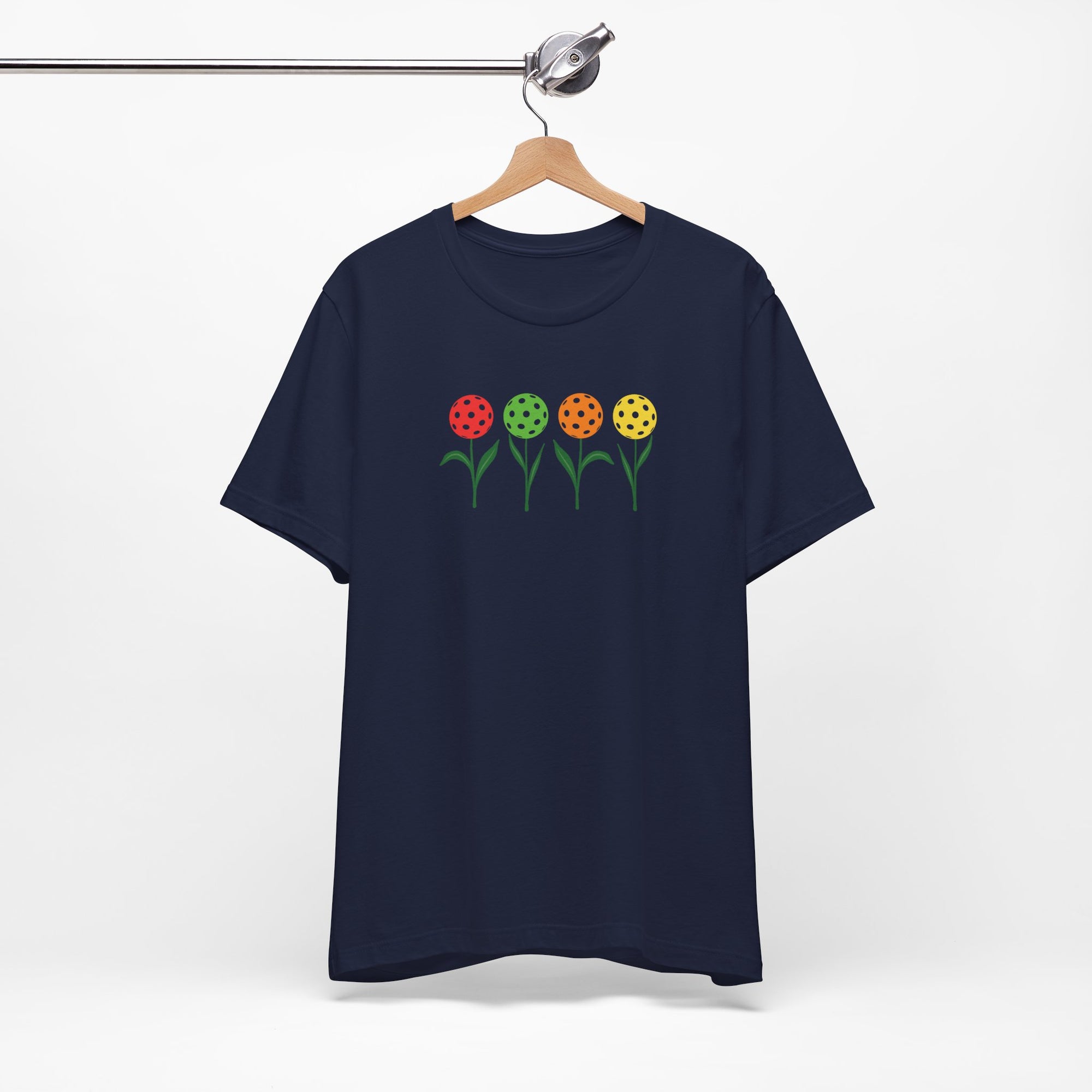Navy blue t-shirt with colorful flowers made from pickleballs on green stems with leaves, on a hanger against a white background