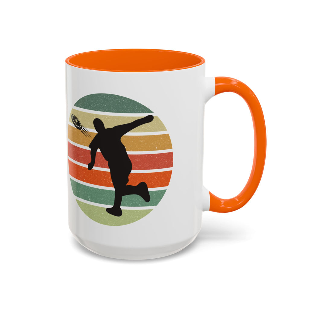 White ceramic coffee mug with orange accents on the handle and inside. The mug features a graphic of a silhouette of a disc golf player above a colorful retro design.