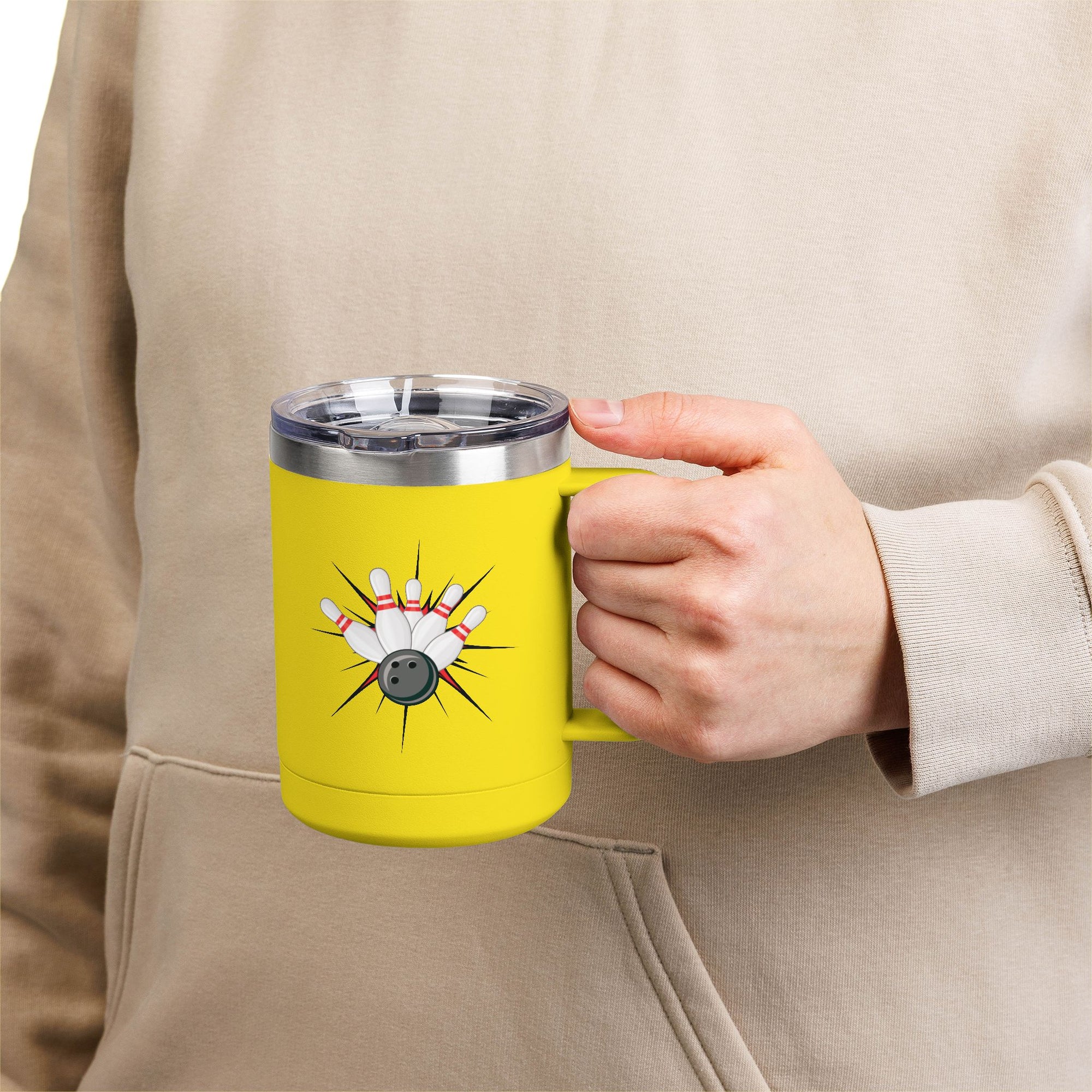 A person holding a yellow travel coffee tumbler mug with a lid and handle, with a graphic design of a bowling ball smashing into pins on a white background