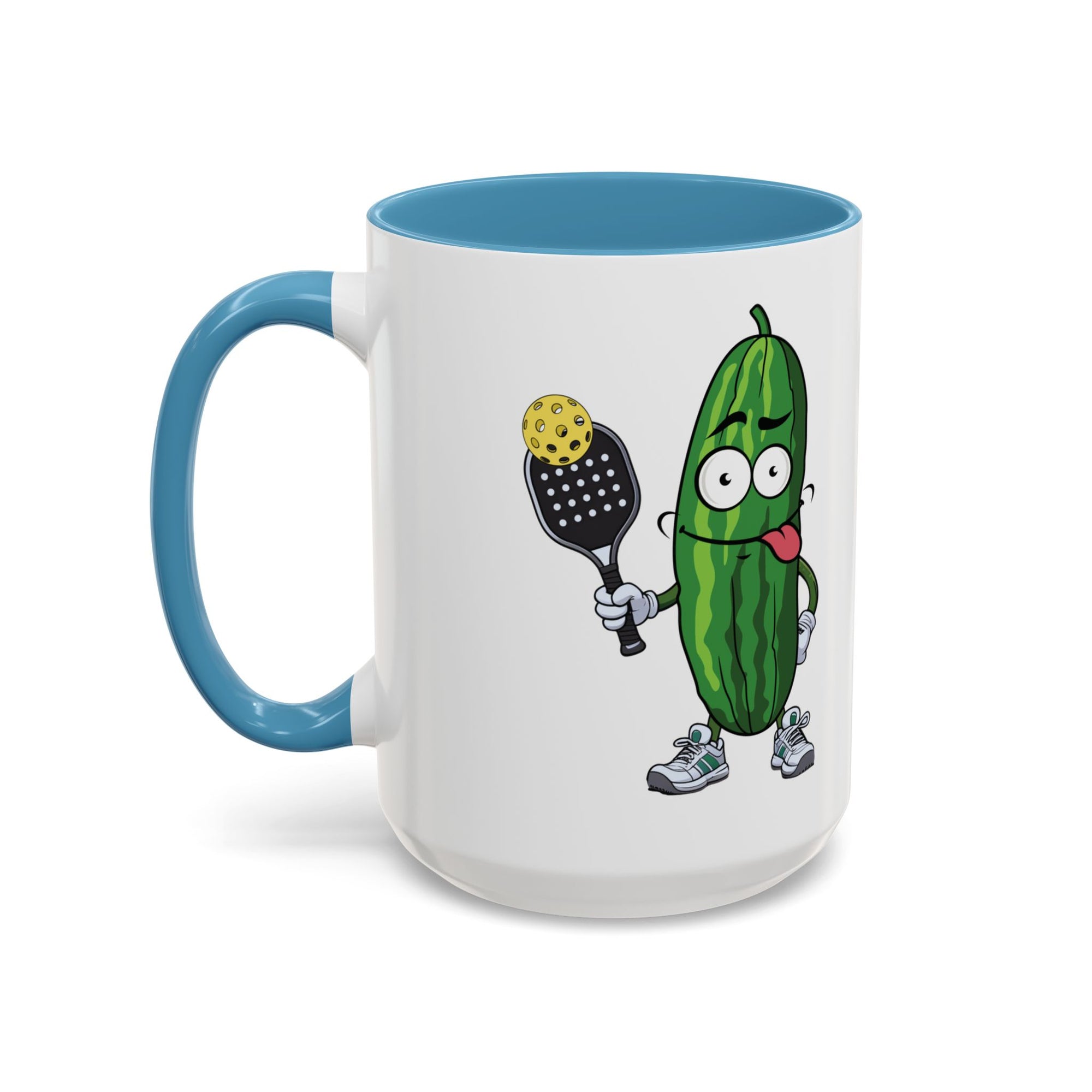 A ceramic coffee mug with light blue accents on the handle and interior, with a cartoon pickle with googly eyes and his tongue sticking out, holding a pickleball paddle with a yellow pickleball, against a white background