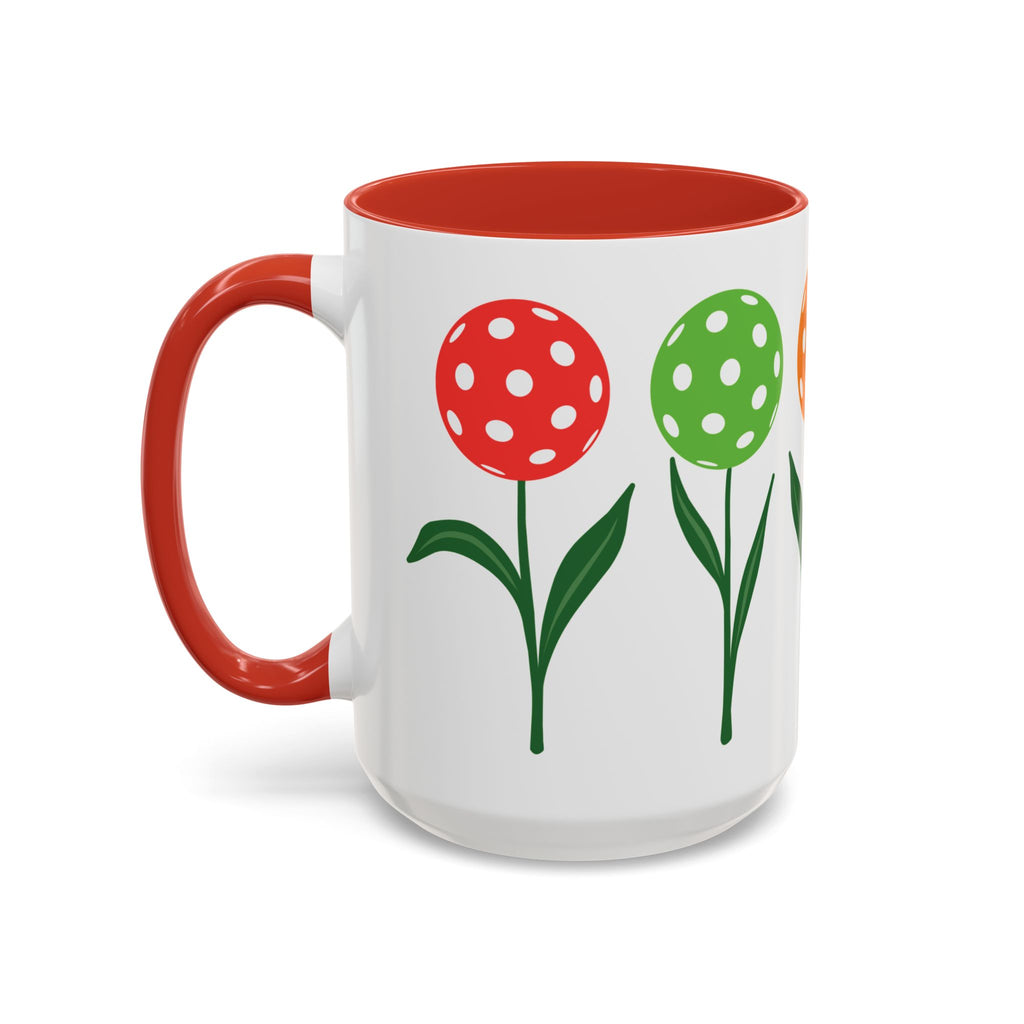 A ceramic coffee mug with red accents on the handle and interior, with colorful flowers made from pickleballs on green stems with leaves, against a white background