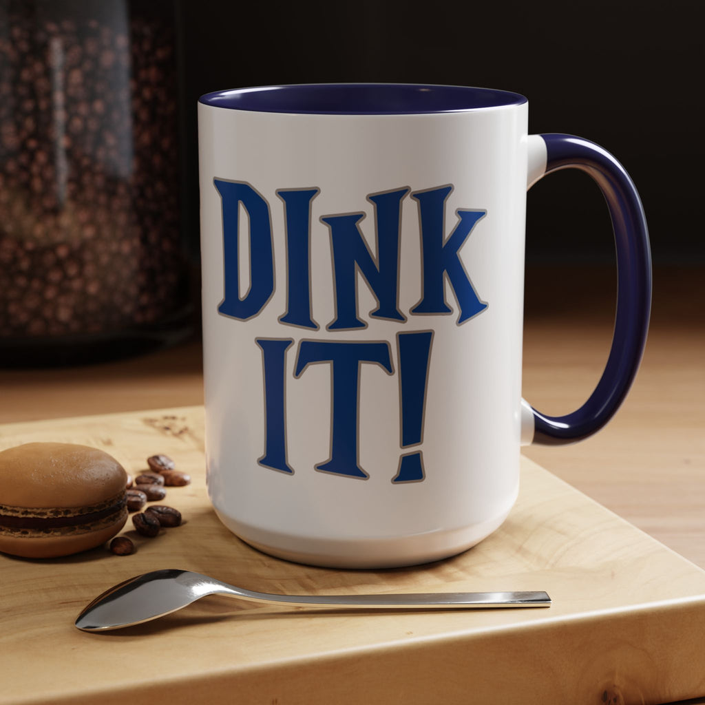 A ceramic coffee mug with blue accents on the handle and interior, with 'DINK IT!' text in blue and outlined in gray, in a coffee shop setting