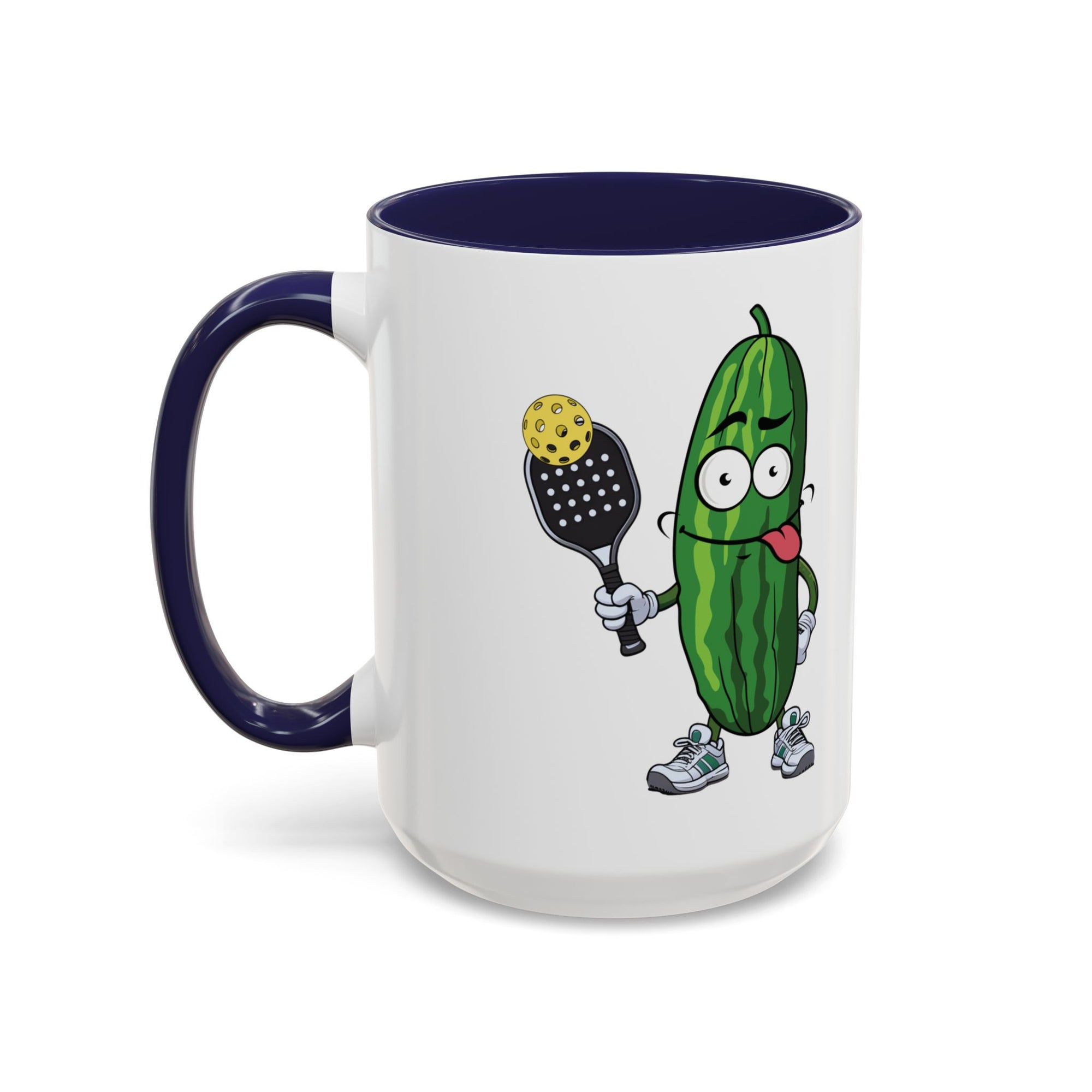 A ceramic coffee mug with dark blue accents on the handle and interior, with a cartoon pickle with googly eyes and his tongue sticking out, holding a pickleball paddle with a yellow pickleball, against a white background