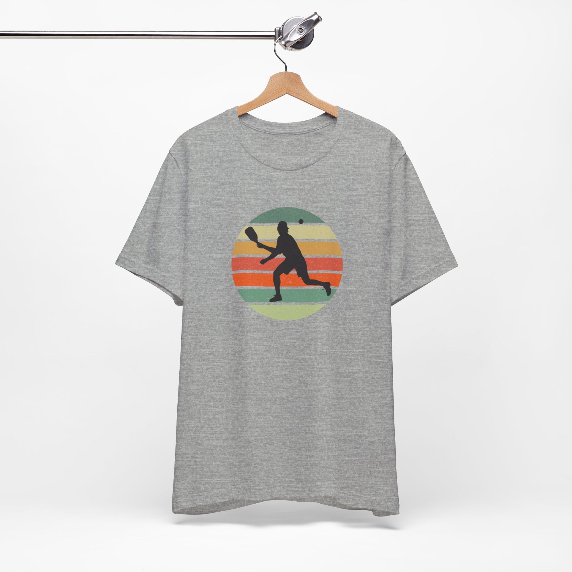 Gray t-shirt with a colorful graphic of a person playing pickleball on a hanger against a white background