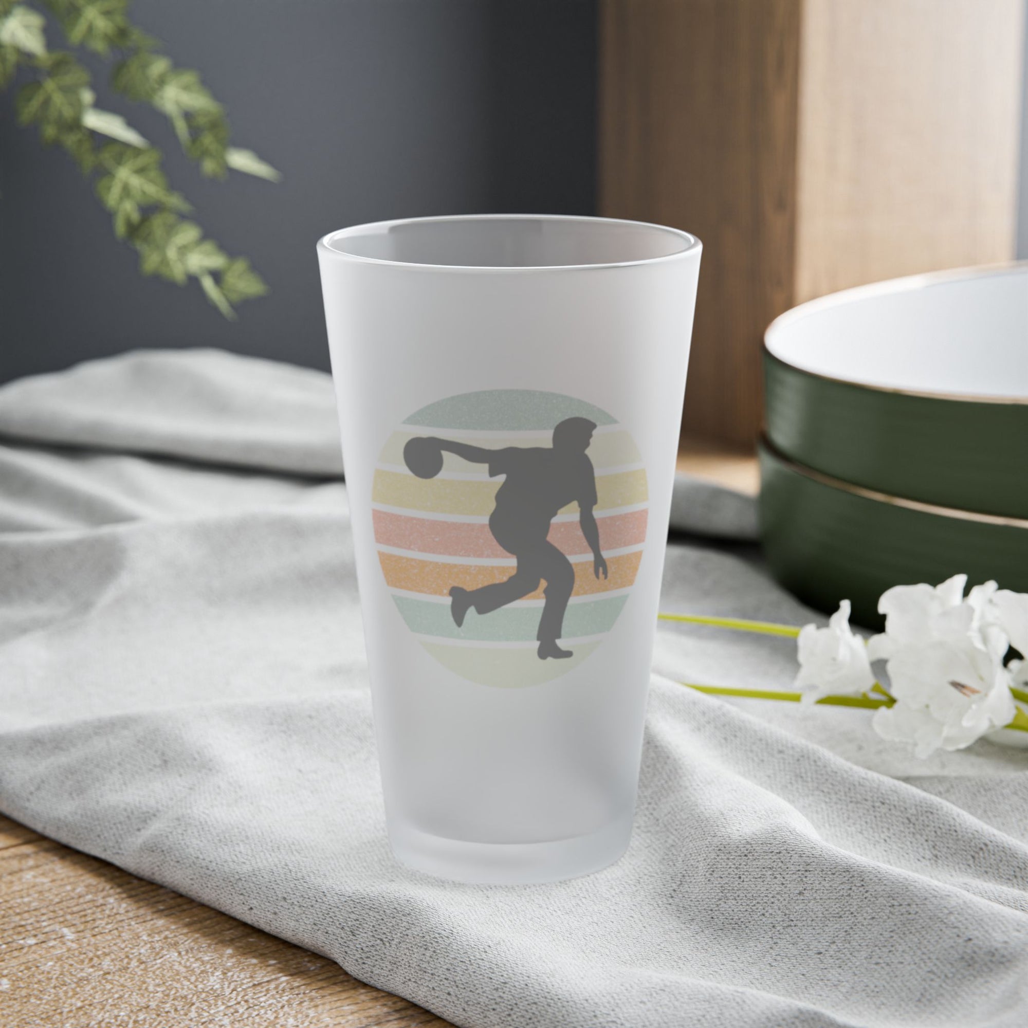 Frosted pint glass with a silhouette of a person bowling on a tabletop