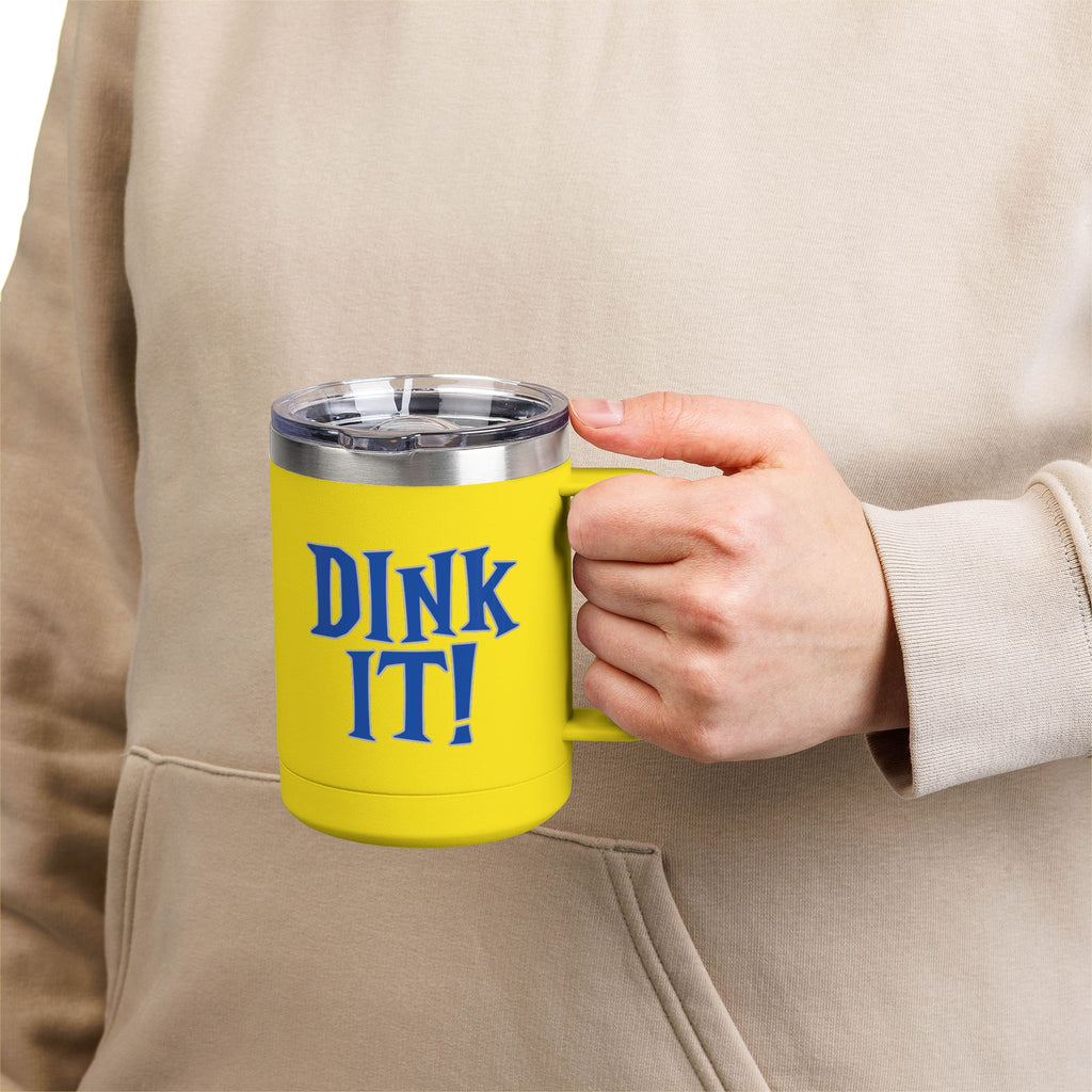 A person holding a yellow stainless steel tumbler with handle and lid featuring the words 'DINK IT!' text in blue and outlined in gray, against a white background