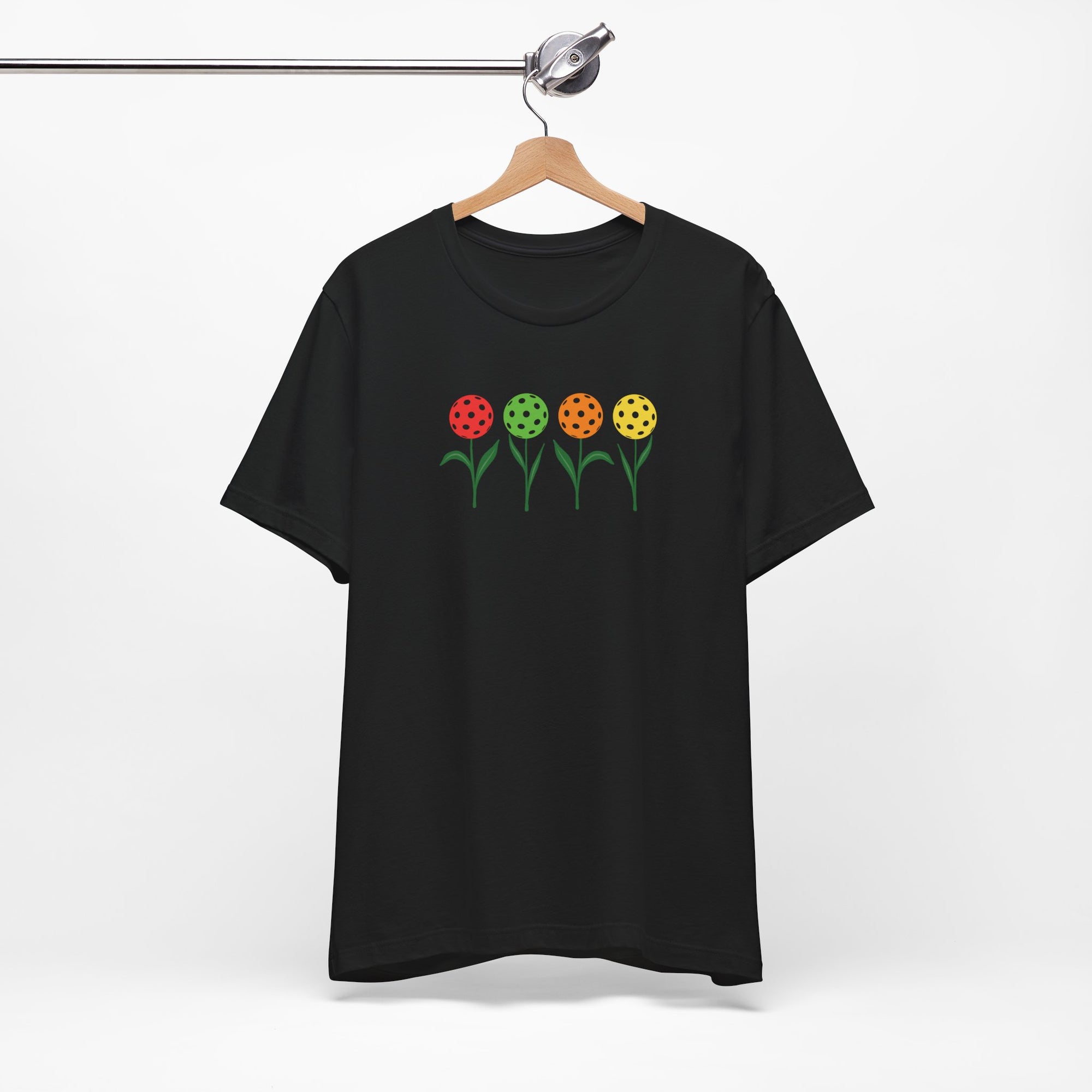 Black t-shirt with colorful flowers made from pickleballs on green stems with leaves, on a hanger against a white background