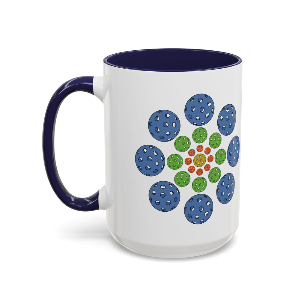 A ceramic coffee mug with dark blue accents on the handle and interior, with a colorful geometric design of pickleballs against a white background