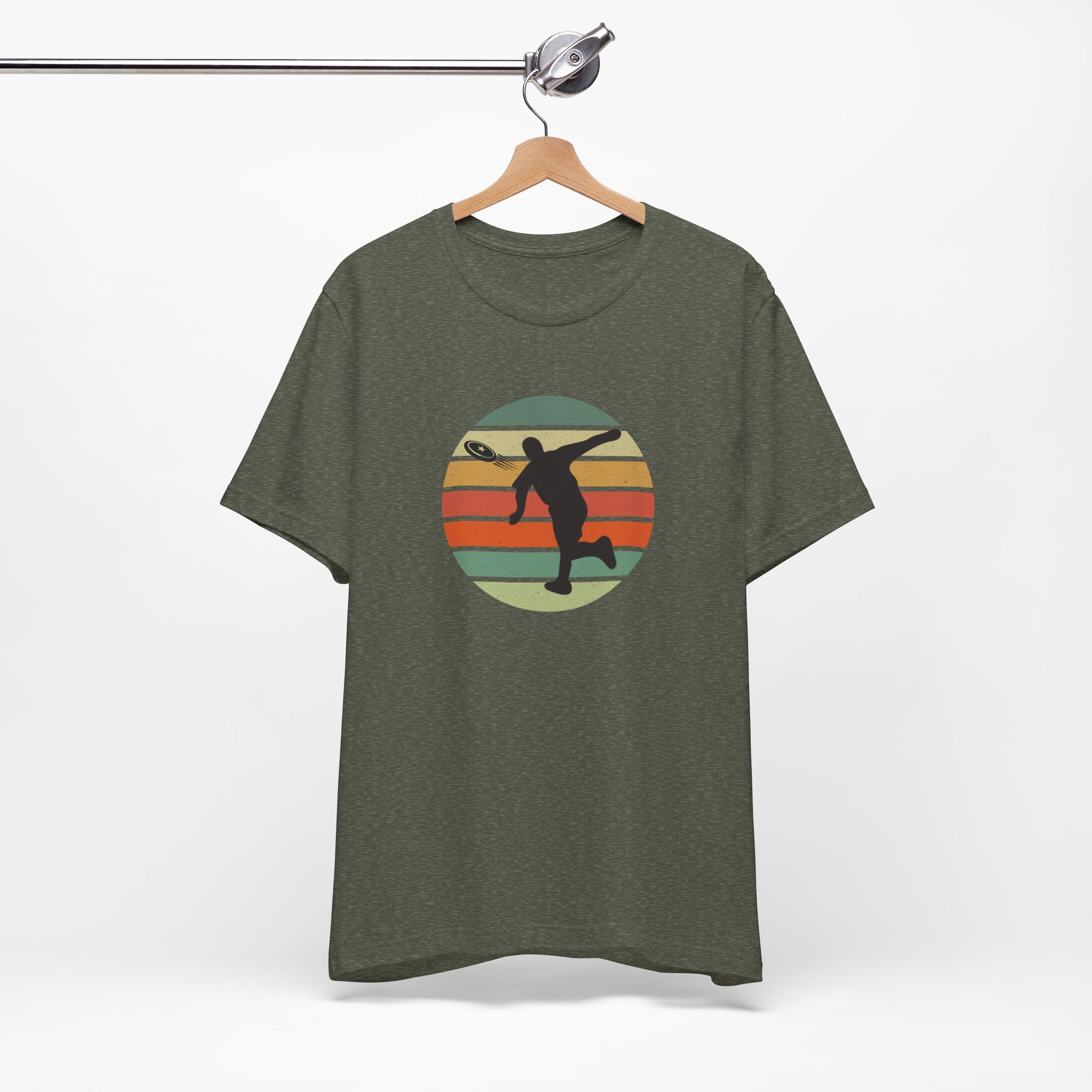 Military green t-shirt with a graphic of a silhouette disc golf player throwing a disc above a colorful retro graphic, hanging on a wooden hanger.