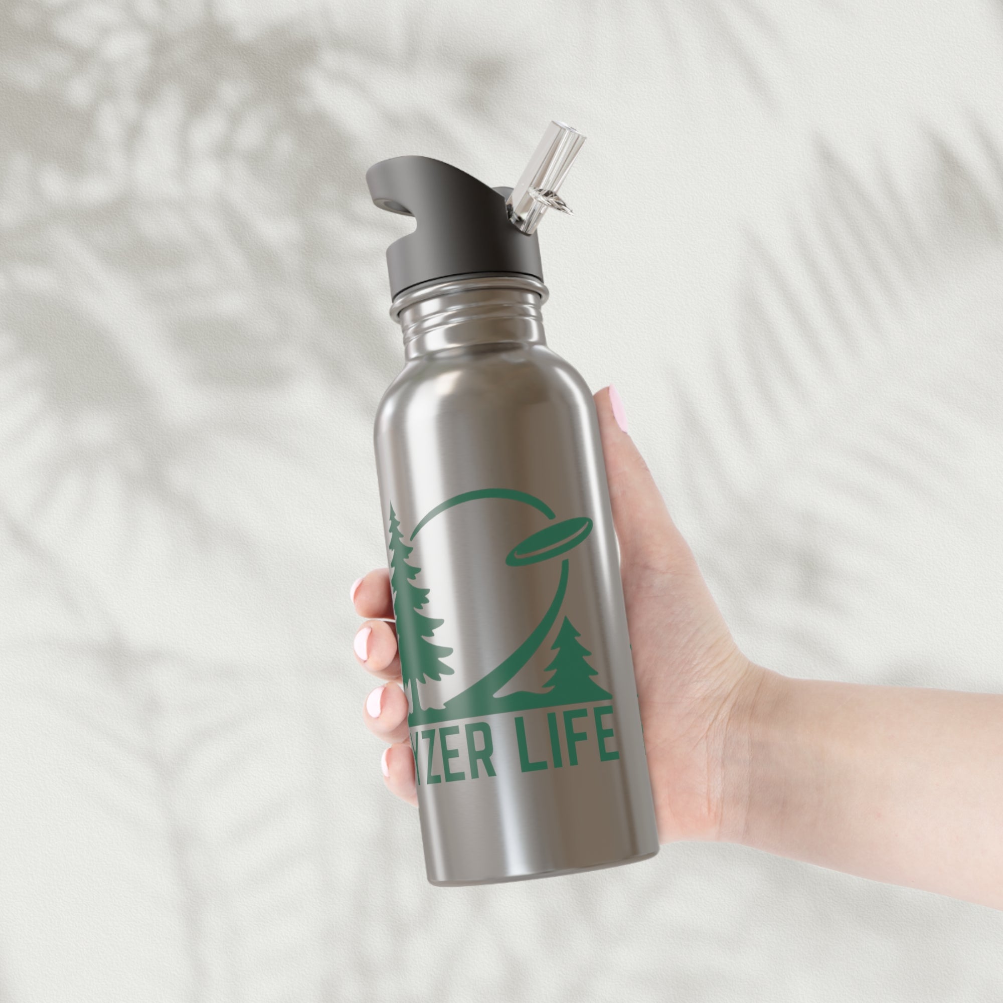 Person holding a stainless steel water bottle with lid with green graphic of trees and a disc golf flying with the words 'HYZER LIFE' below the image, on a white background.