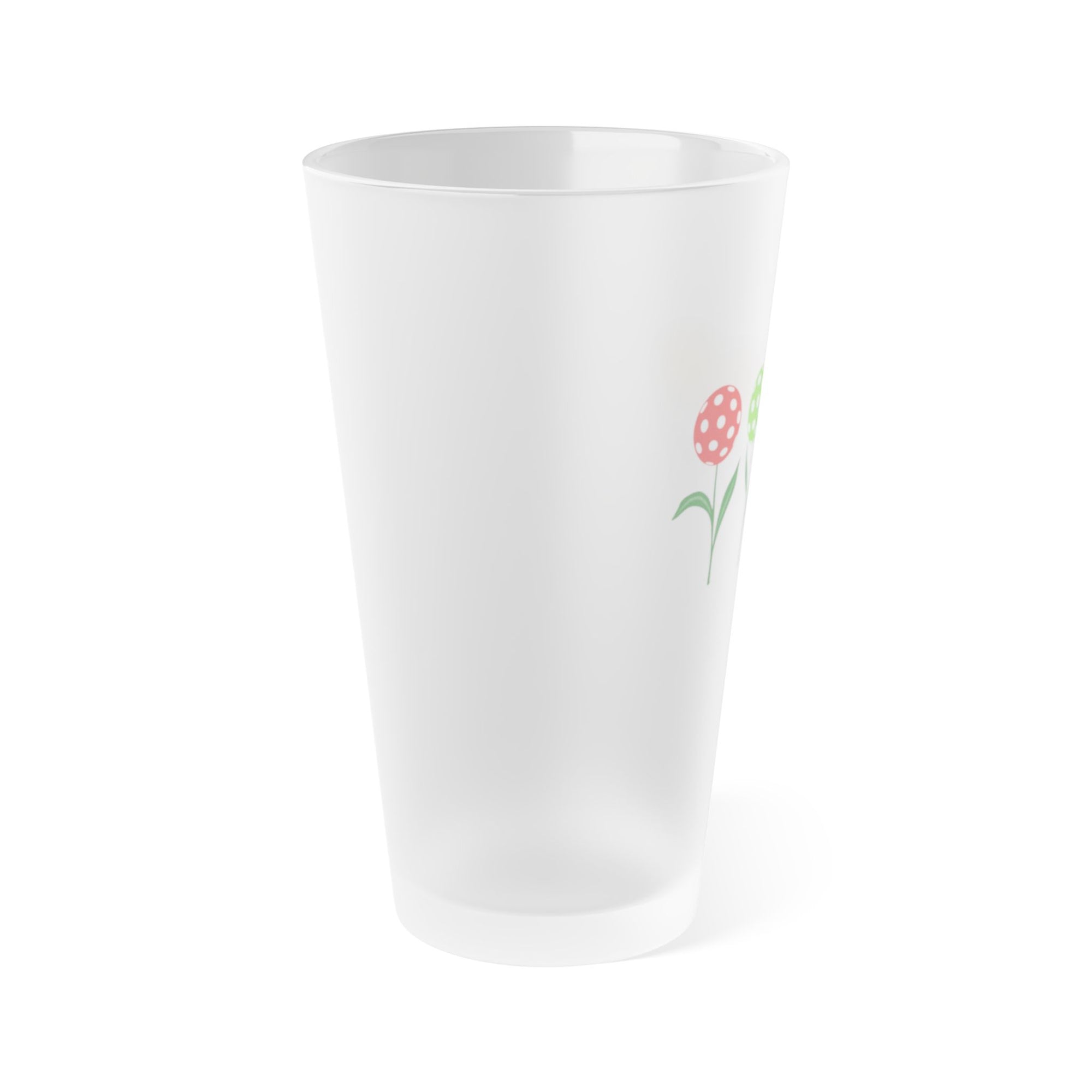 Side view of a frosted pint glass with four colorful flowers made out of pickleballs, on a white background.