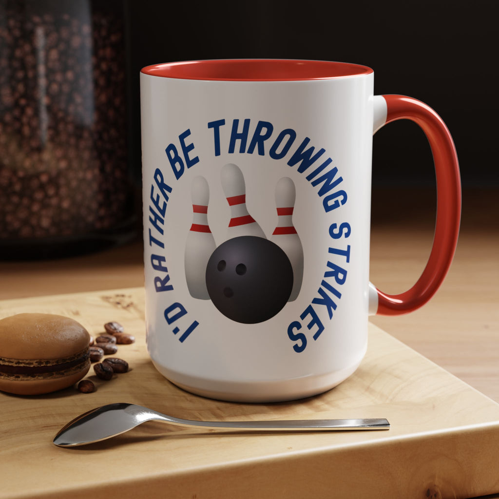 Ceramic coffee mug with red accents on the handle and interior, with bowling pins and a bowling ball and text saying "I'd Rather Be Throwing Strikes" in a coffee shop setting.