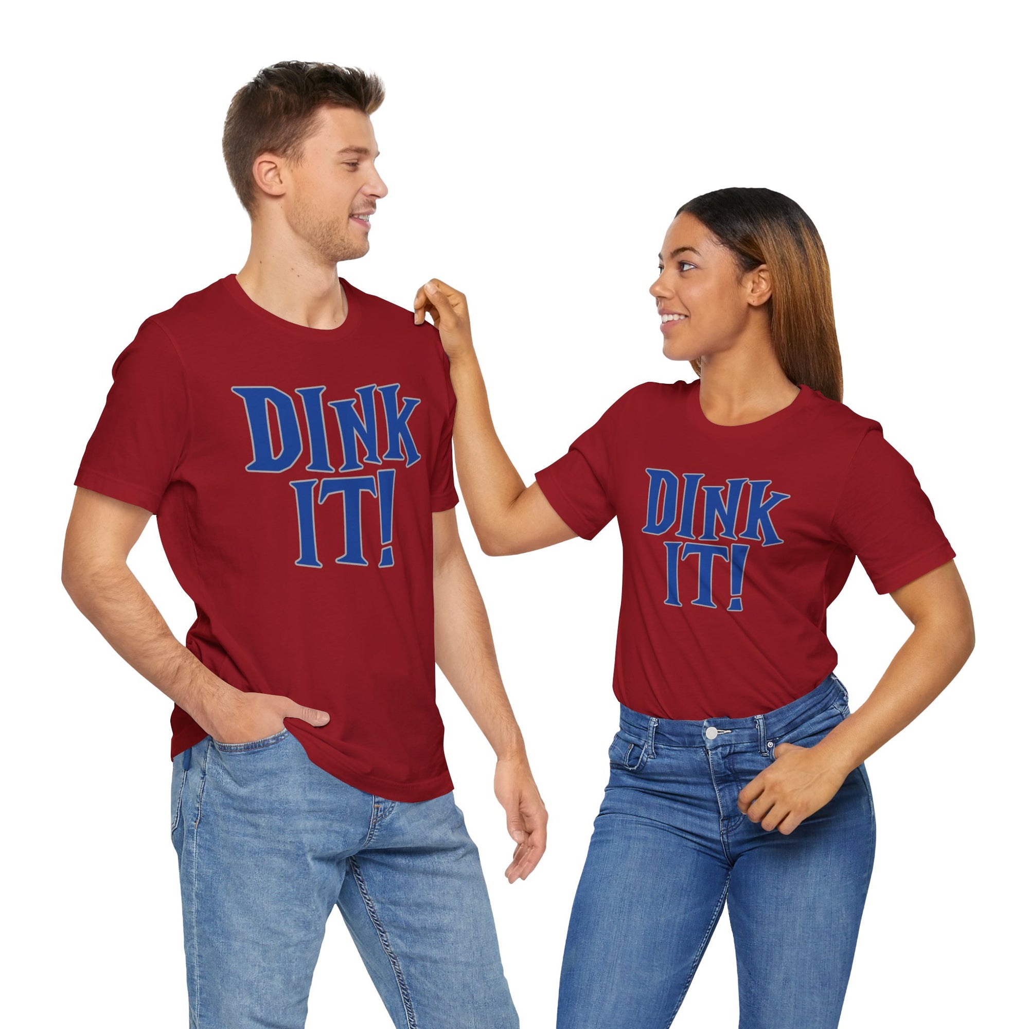 A man and a woman each wearing a red t-shirt with 'DINK IT!' text in blue and outlined in gray, on a hanger against a white background