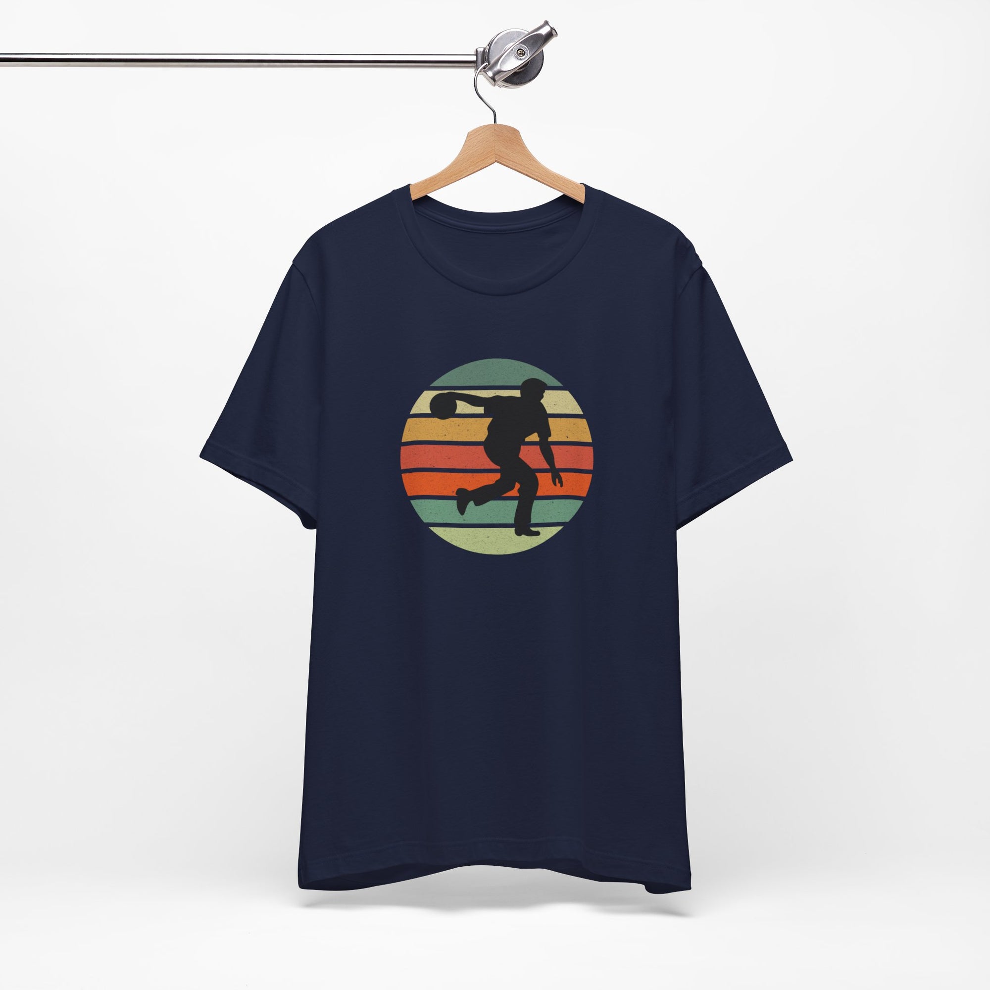Navy blue t-shirt with a graphic of a silhouette of a bowler over a colorful retro image, hanging on a wooden hanger against a white background.