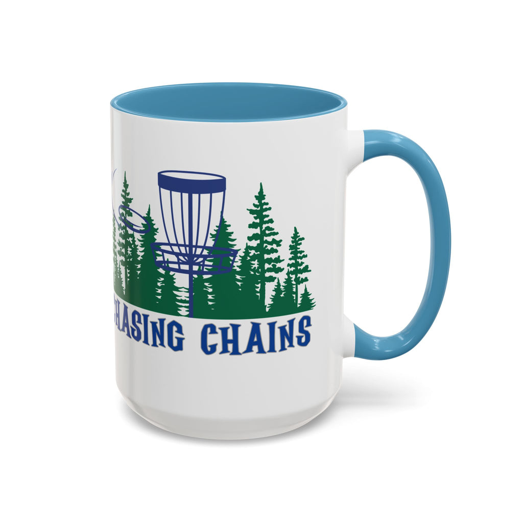 A ceramic coffee mug with light blue accents on the handle and interior, with 'Chasing Chains' graphic featuring a flying disc golf disc and basket and chains in front of a scenic evergreen tree landscape, against a white background