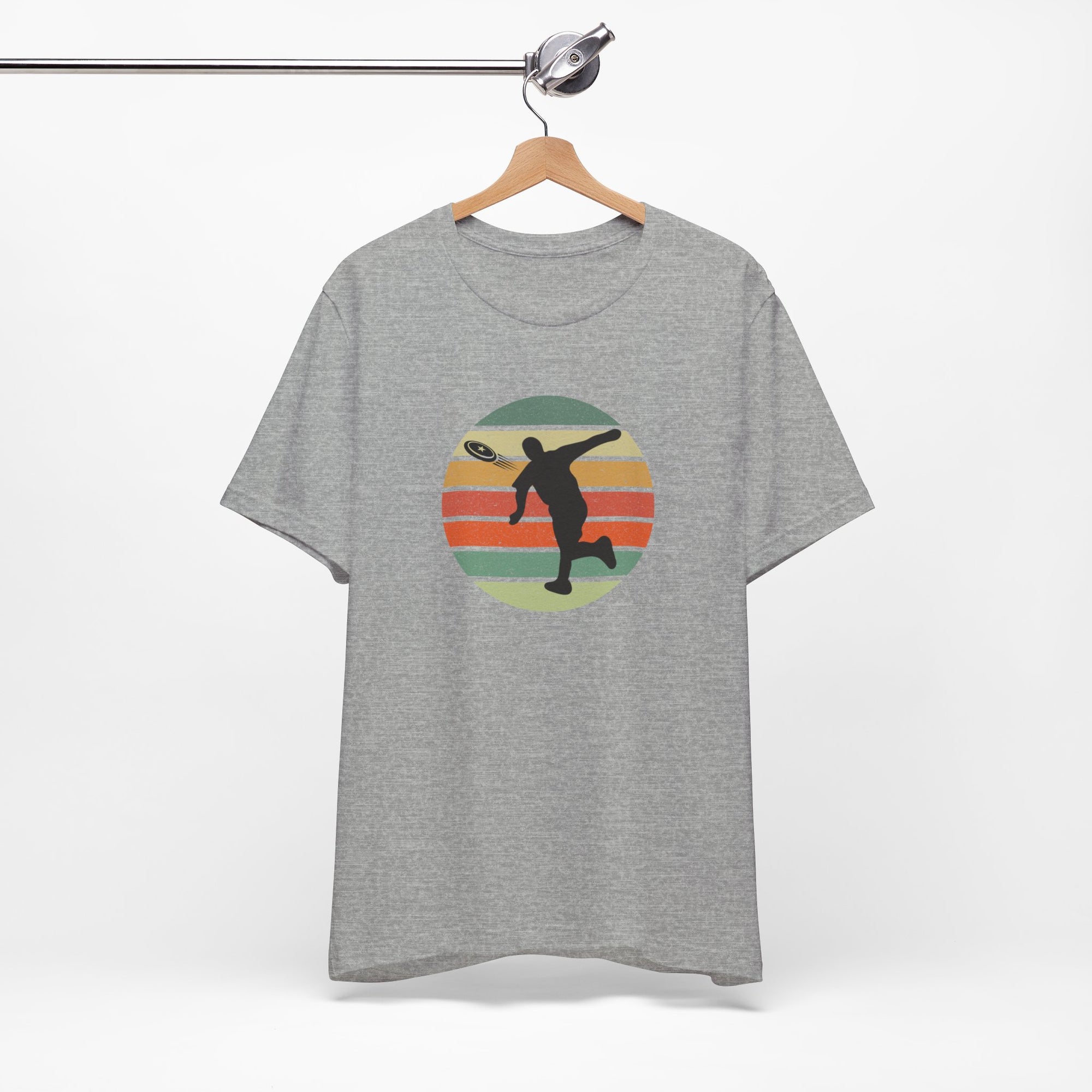 Light gray t-shirt with a graphic of a silhouette disc golf player throwing a disc above a colorful retro graphic, hanging on a wooden hanger.