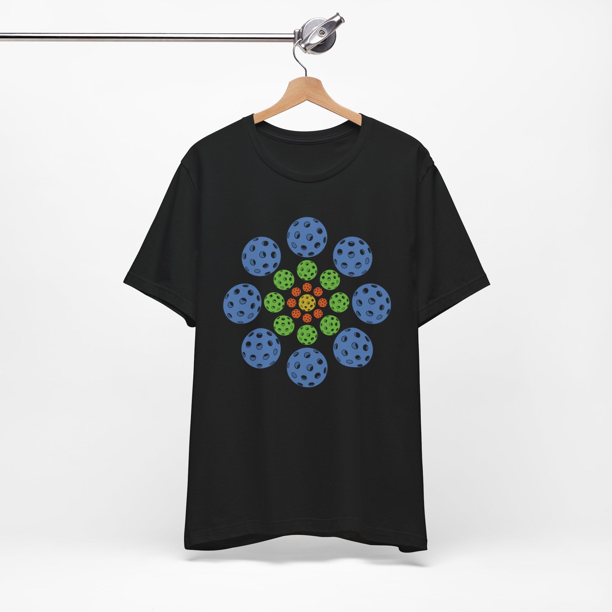 Black t-shirt with colorful geometric design of pickleballs on a hanger against a white background