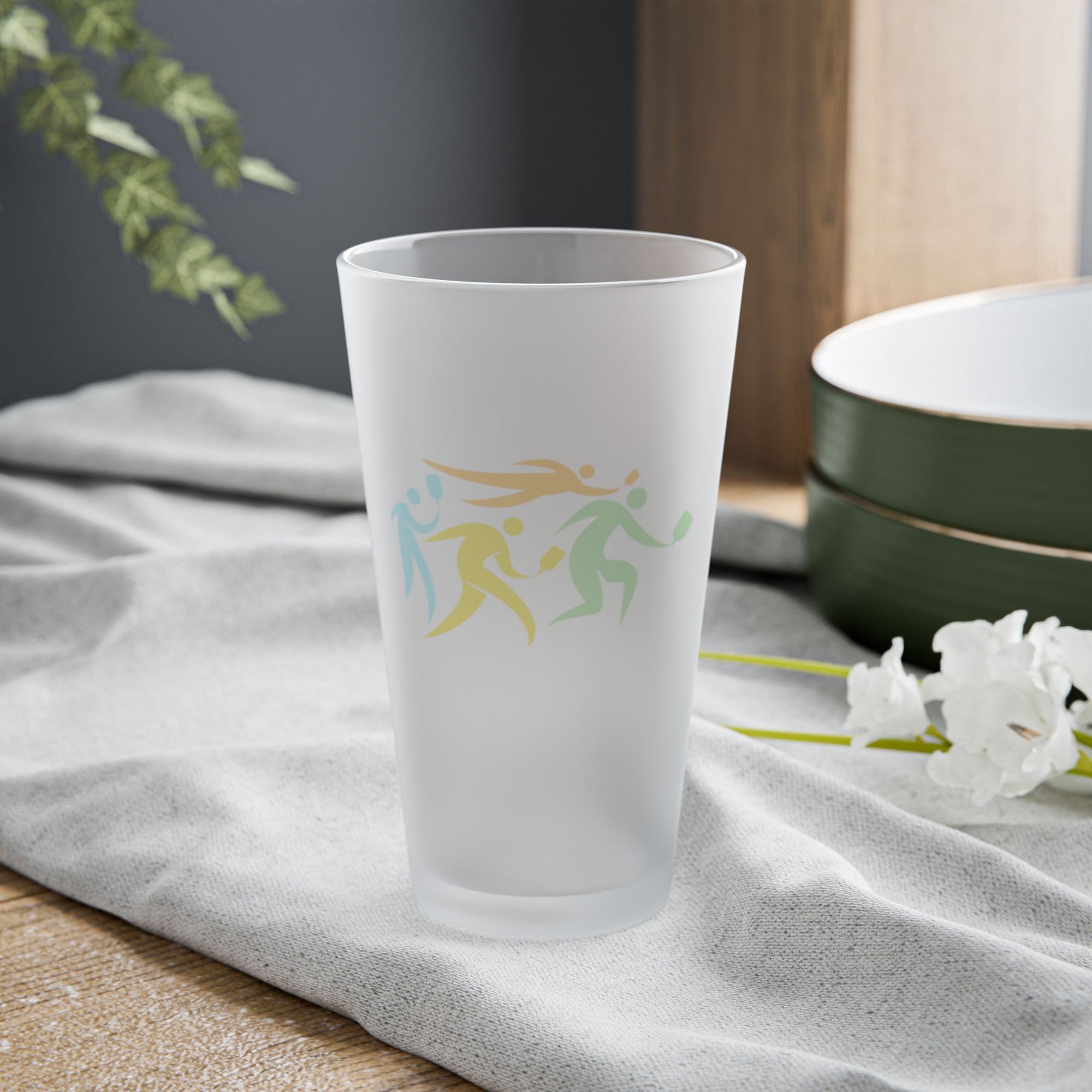 Frosted pint glass with images of four pickleball players in action, on a tabletop