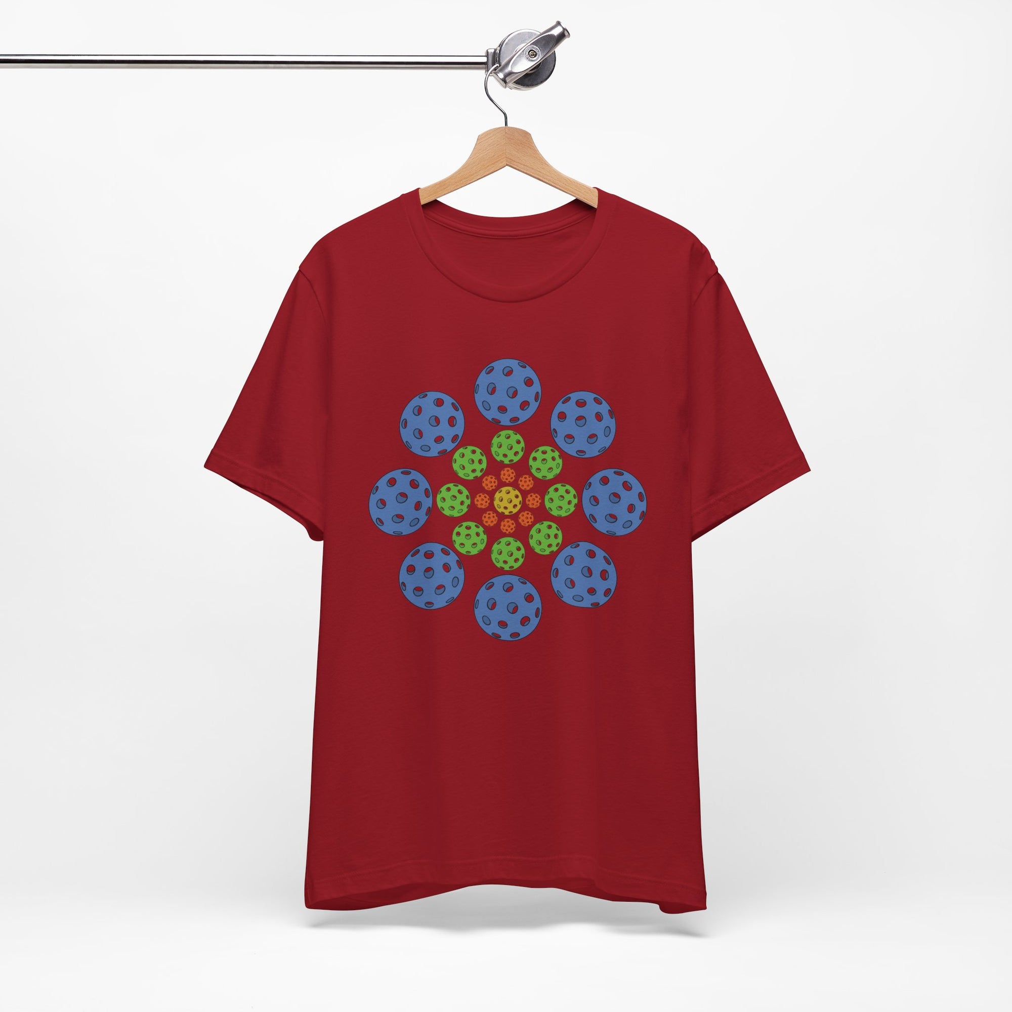 Maroon t-shirt with colorful geometric design of pickleballs on a hanger against a white background