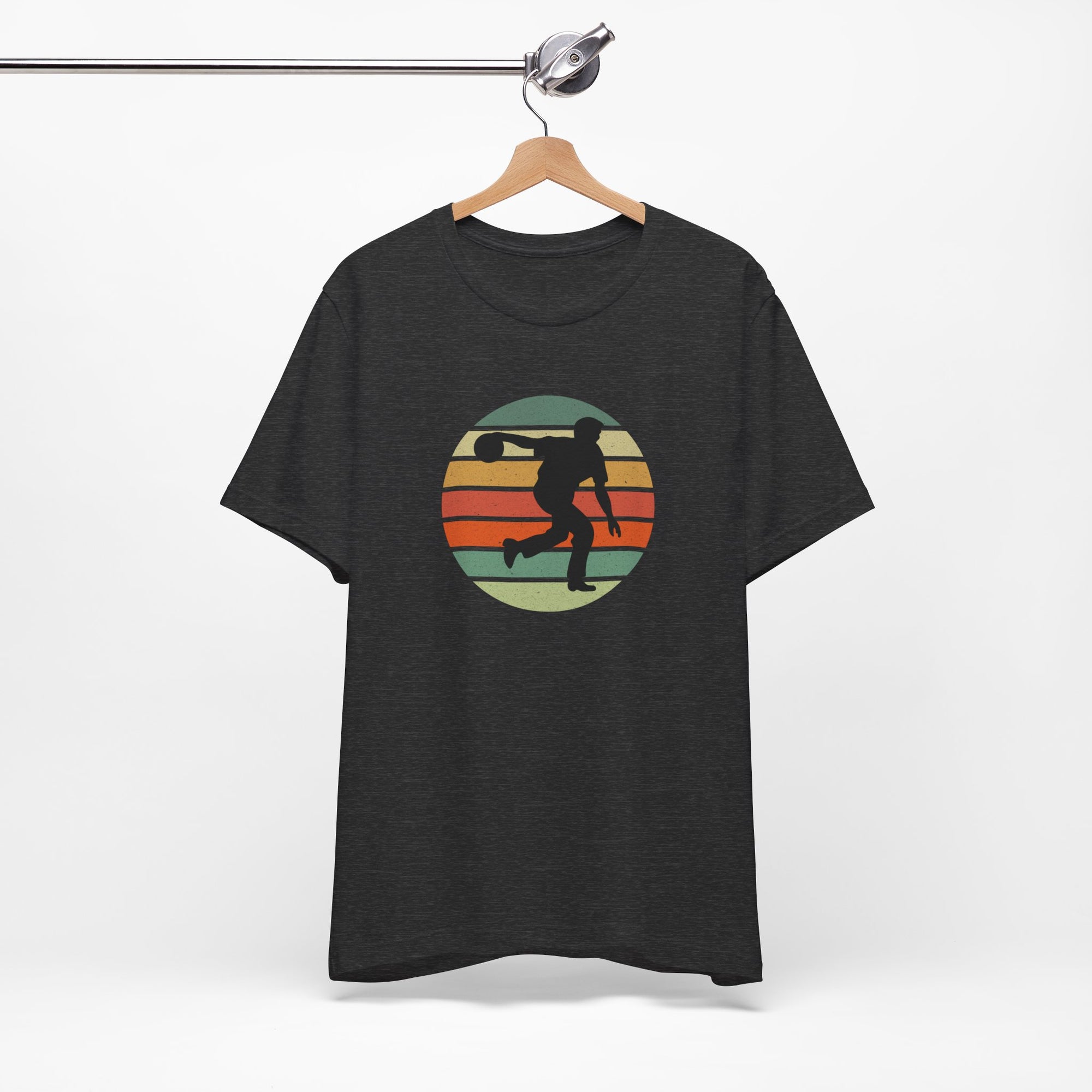 Dark gray t-shirt with a graphic of a silhouette of a bowler over a colorful retro image, hanging on a wooden hanger against a white background.