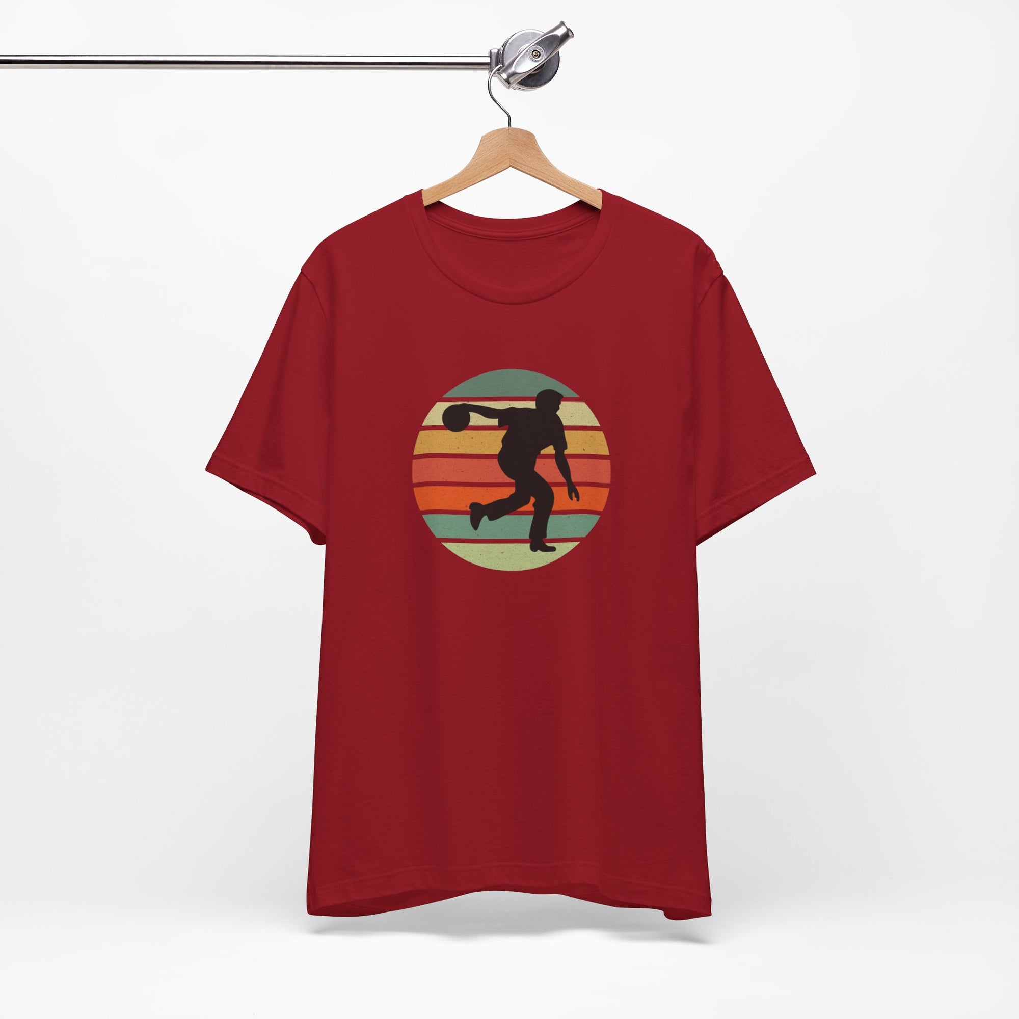 Red t-shirt with a graphic of a silhouette of a bowler over a colorful retro image, hanging on a wooden hanger against a white background.