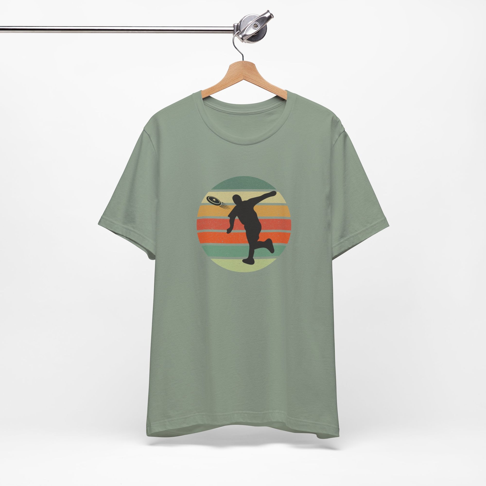 Teal t-shirt with a graphic of a silhouette disc golf player throwing a disc above a colorful retro graphic, hanging on a wooden hanger.