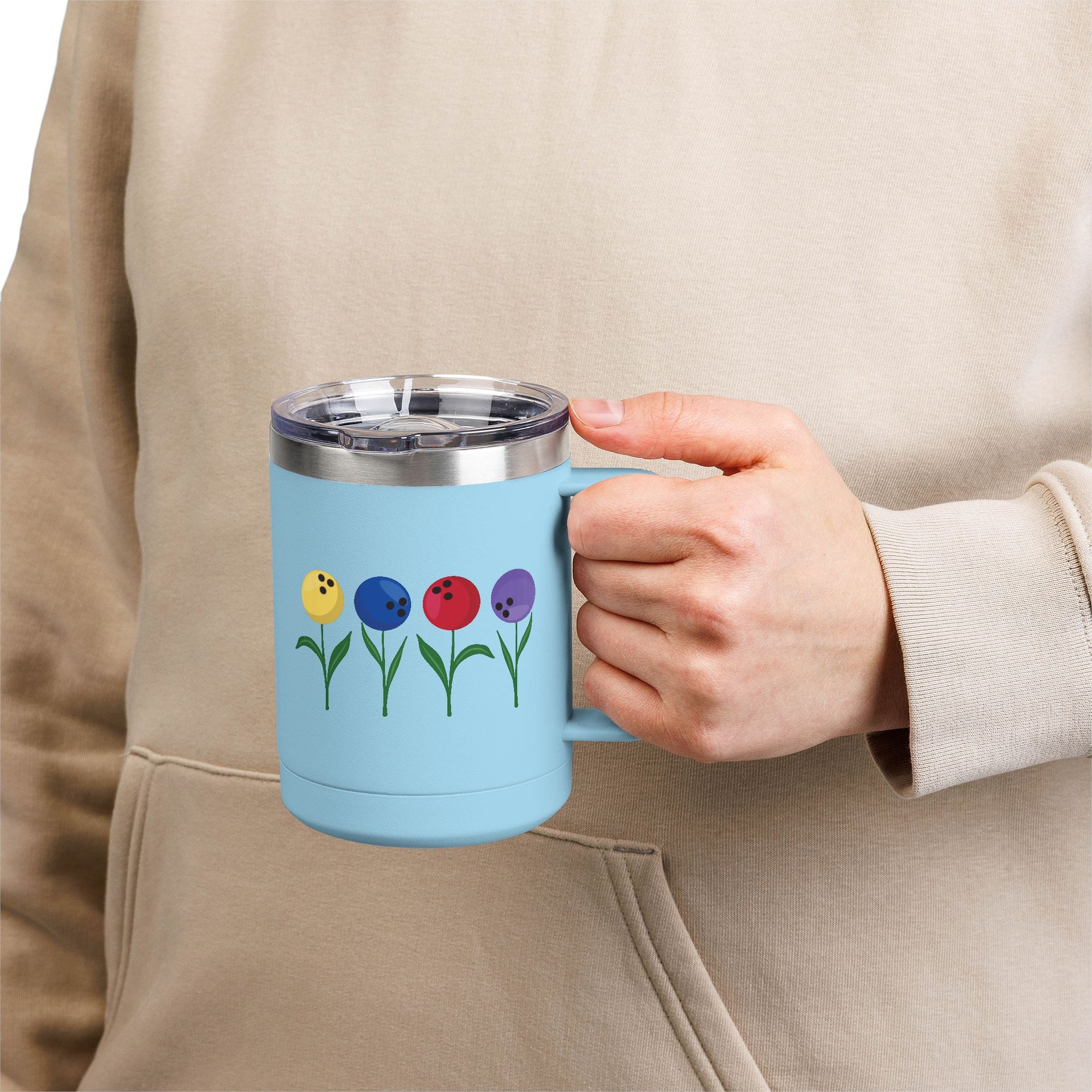 A person holding a light blue travel mug tumbler with lid and handle, with colorful flowers made out of bowling balls