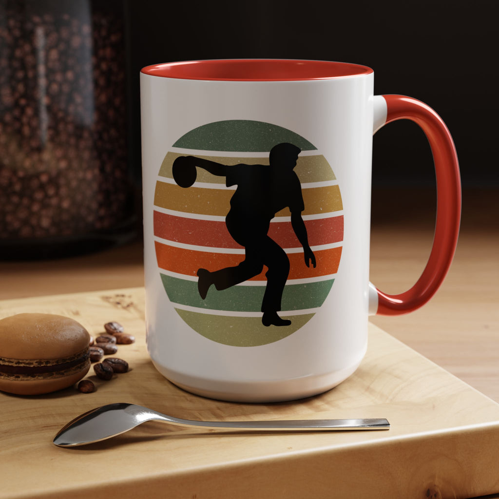 Ceramic coffee mug with red accents on the handle and inside, with a graphic of a silhouette of a bowler over a colorful retro image, in a coffee shop background.