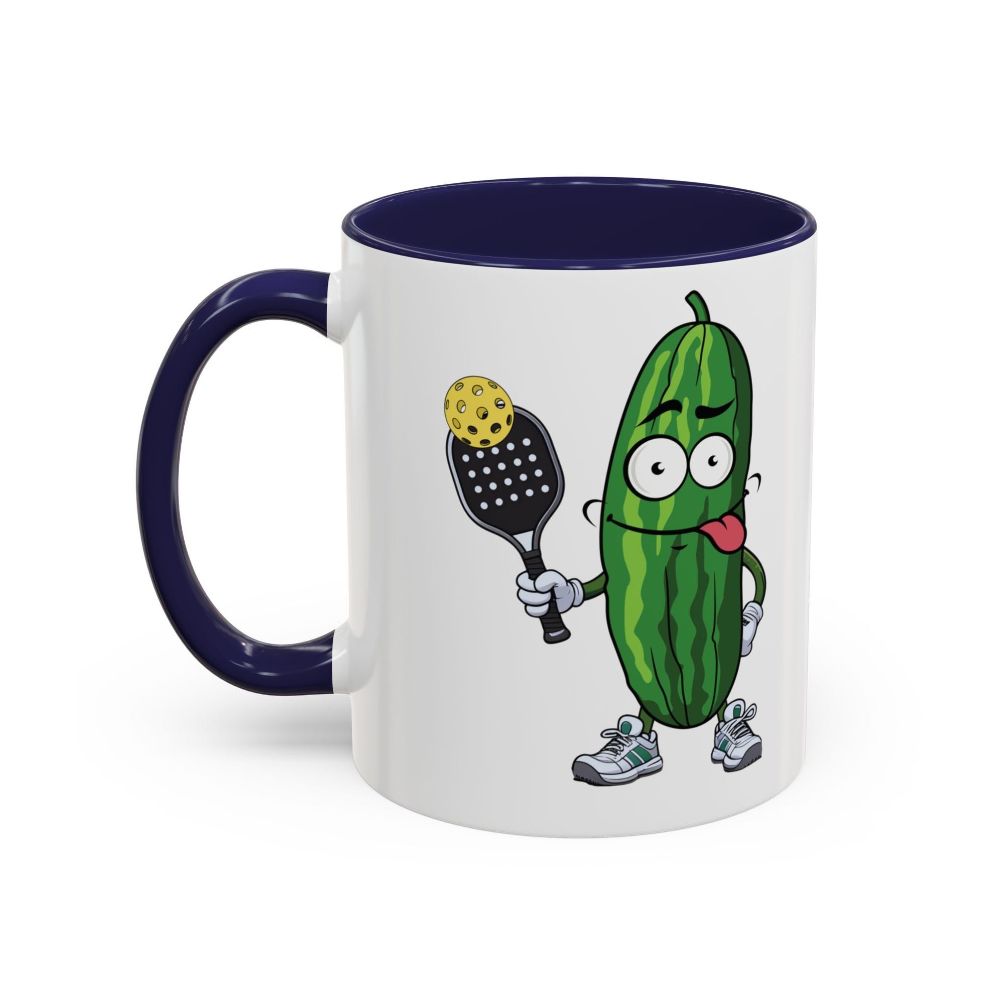 A ceramic coffee mug with dark blue accents on the handle and interior, with a cartoon pickle with googly eyes and his tongue sticking out, holding a pickleball paddle with a yellow pickleball, against a white background