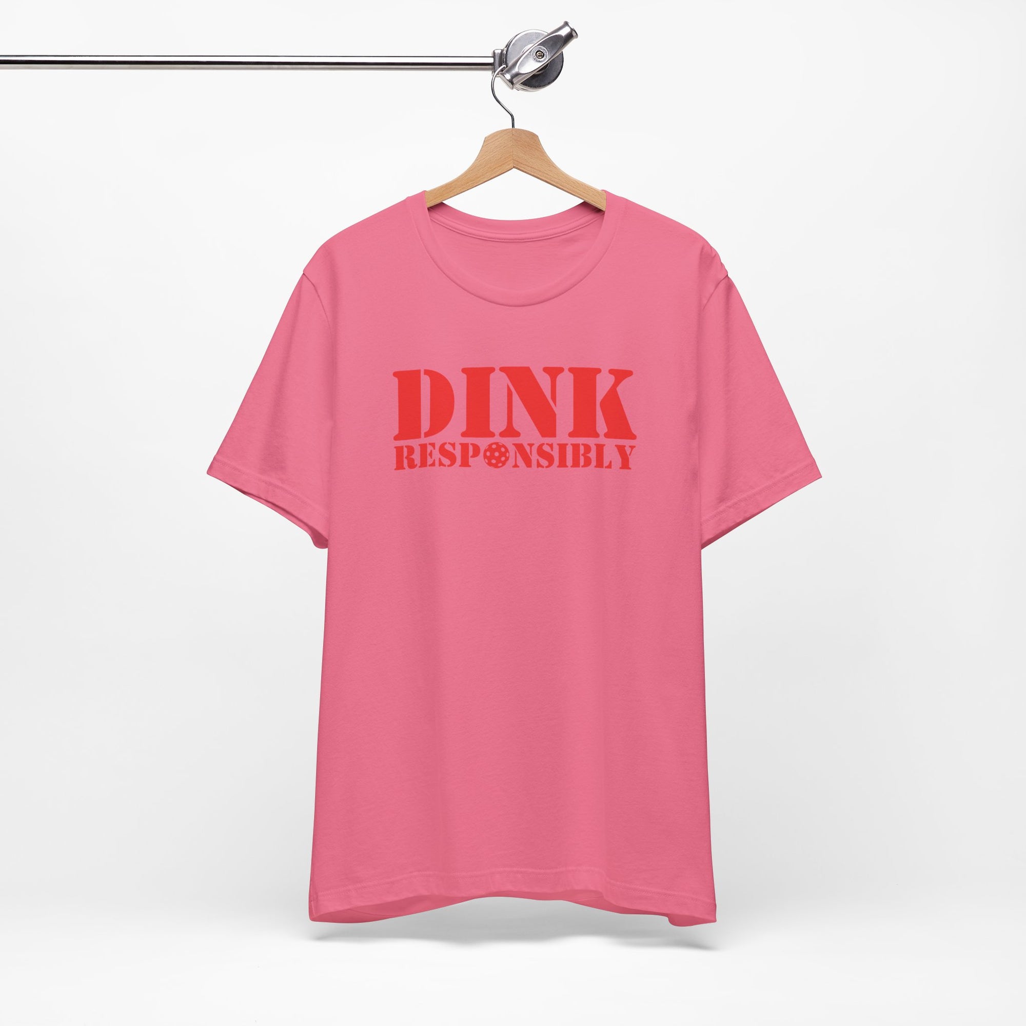 Pink t-shirt with red text 'DINK RESPONSIBLY' with a pickleball replacing the "O" in "Responsibly" on a hanger against a white background