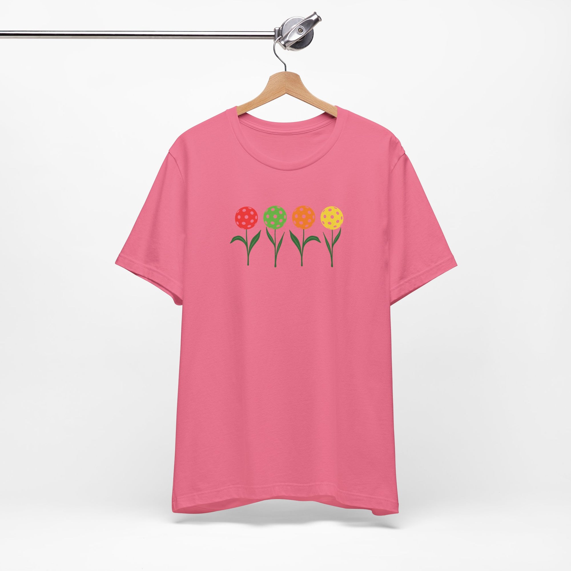 Pink t-shirt with colorful flowers made from pickleballs on green stems with leaves, on a hanger against a white background