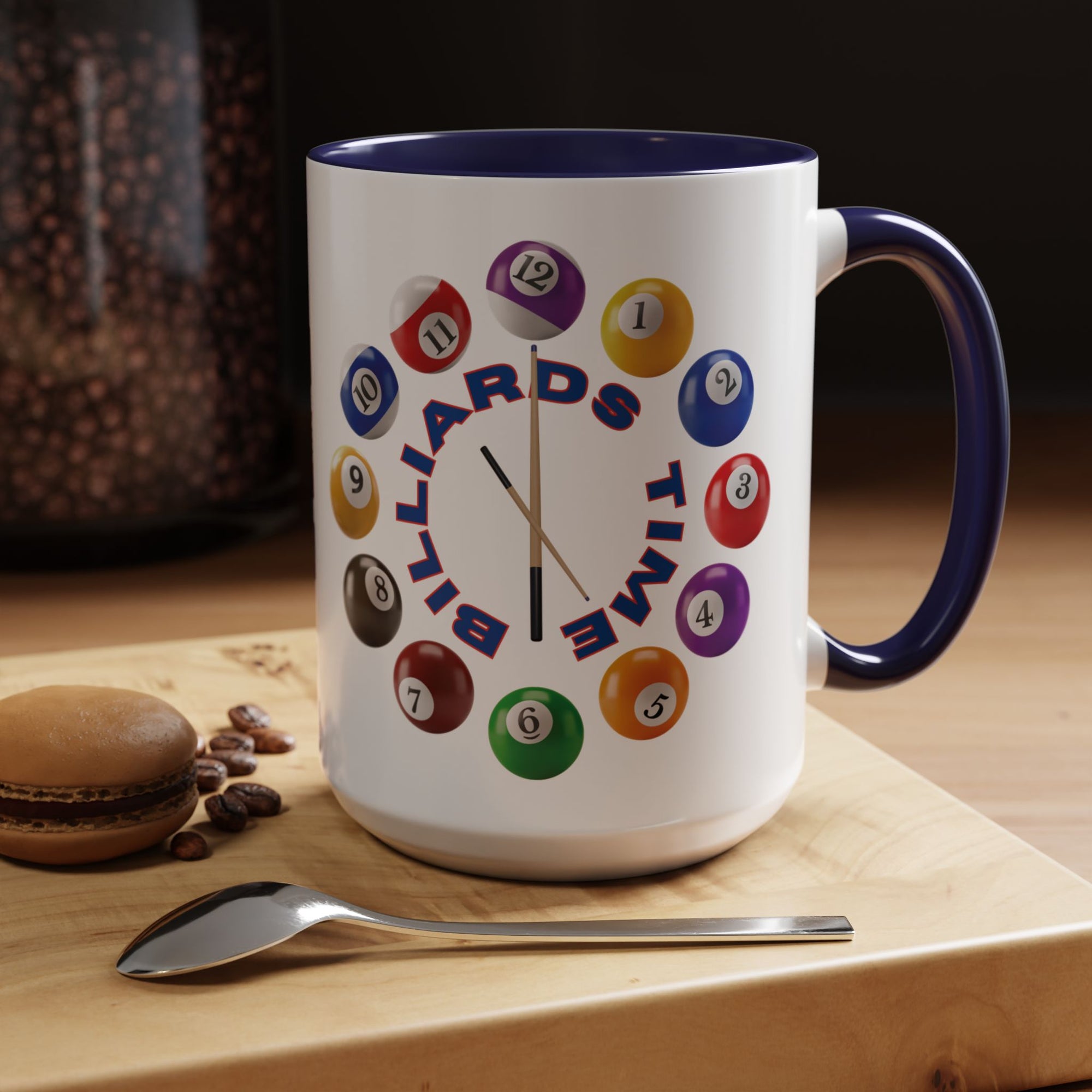 A white ceramic coffee mug with dark blue accents on the handle and interior, with the text "Billiards Time" surrounded by a clock made up of colorful billiard balls and cue sticks, in a coffee shop setting