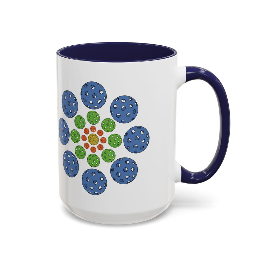 A ceramic coffee mug with dark blue accents on the handle and interior, with a colorful geometric design of pickleballs against a white background