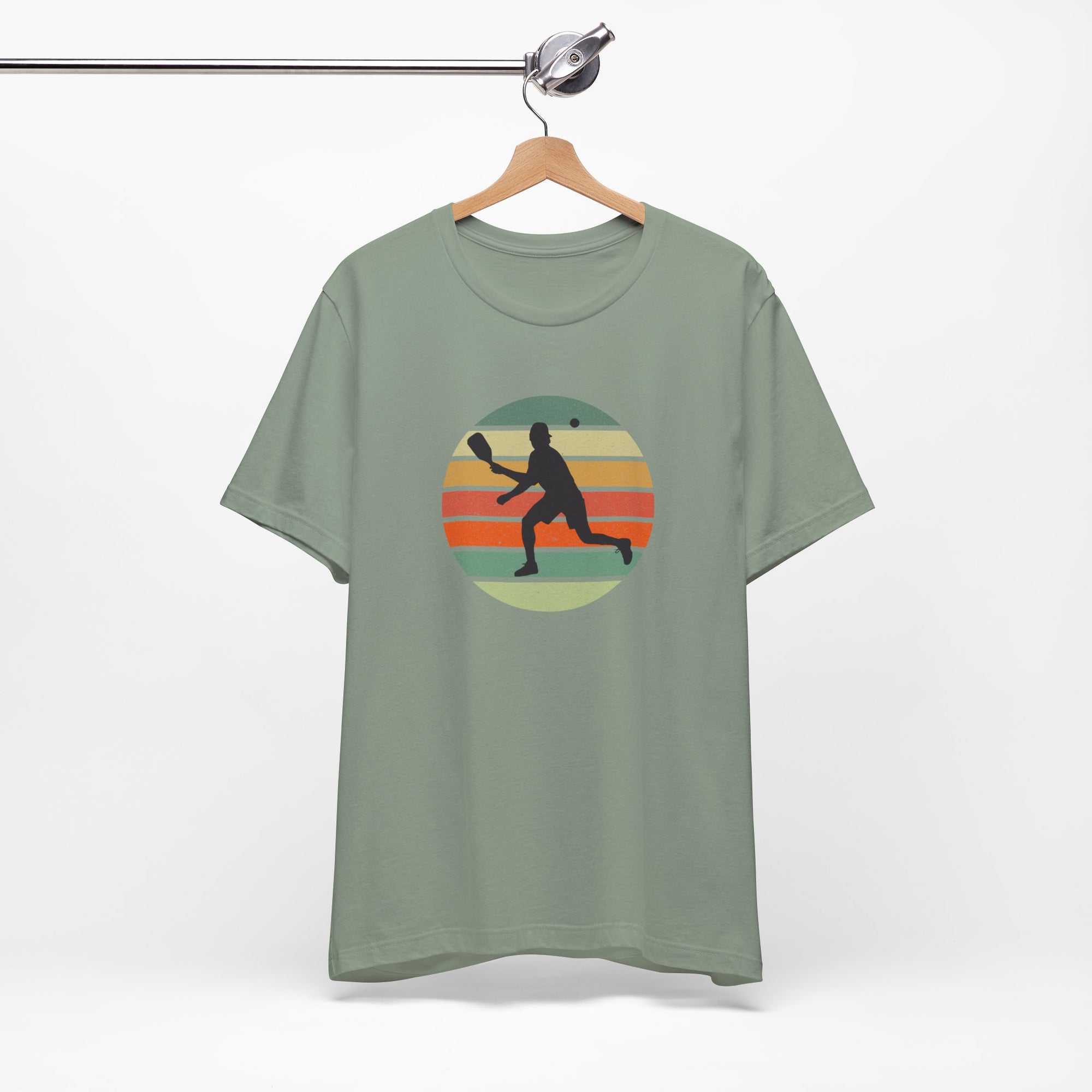 Teal t-shirt with a graphic design of a person playing pickleball on a hanger against a white background