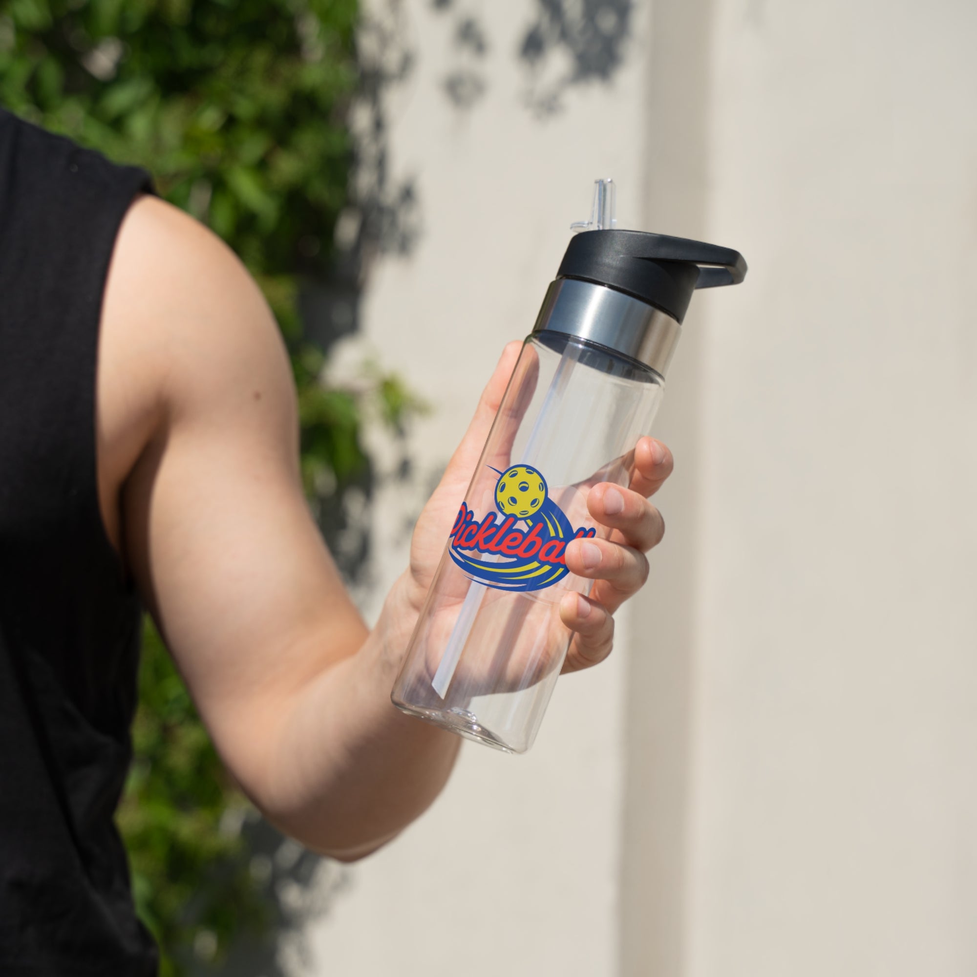 A person holding a clear water bottle with lid with a classic pickleball logo featuring the word pickleball and a yellow pickleball with motion lines, against a white background