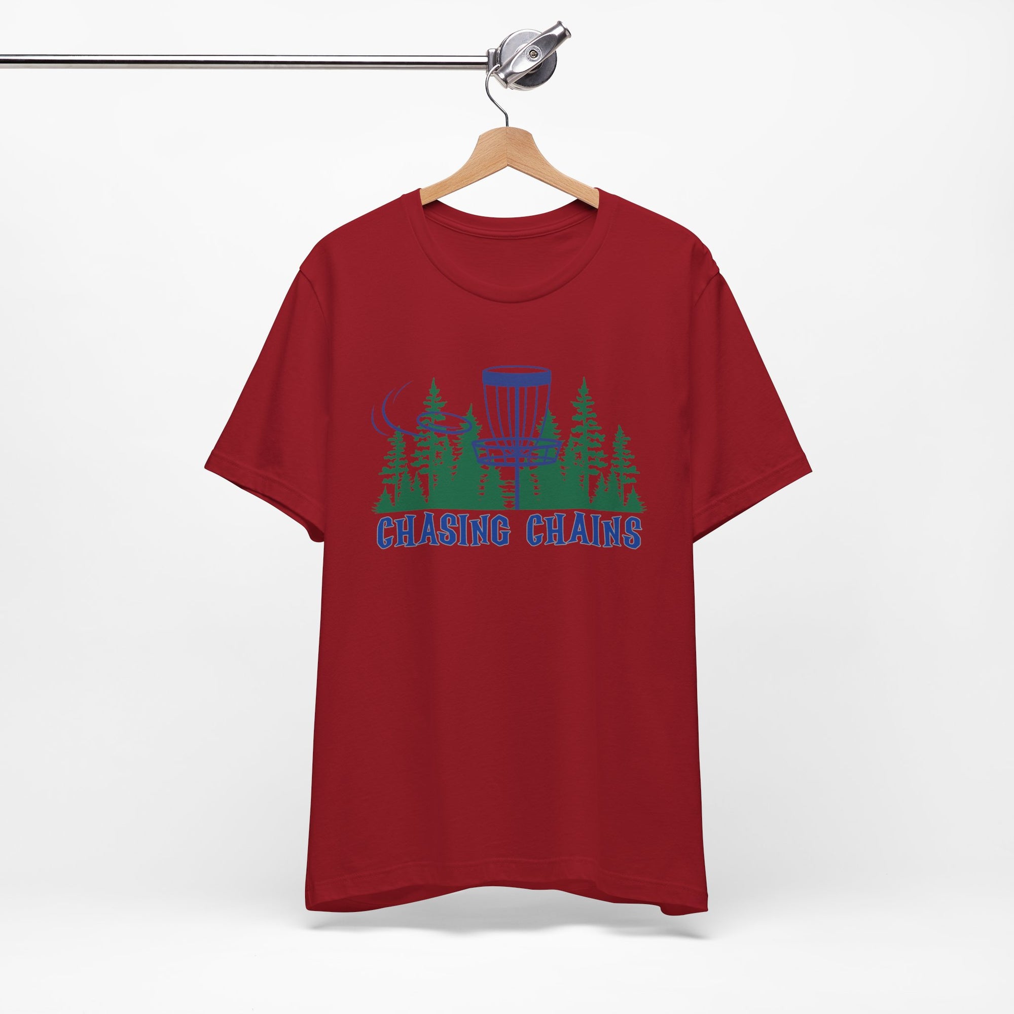 Maroon t-shirt with 'Chasing Chains' graphic featuring a flying disc golf disc and basket and chains in front of a scenic evergreen tree landscape, on a hanger against a white background