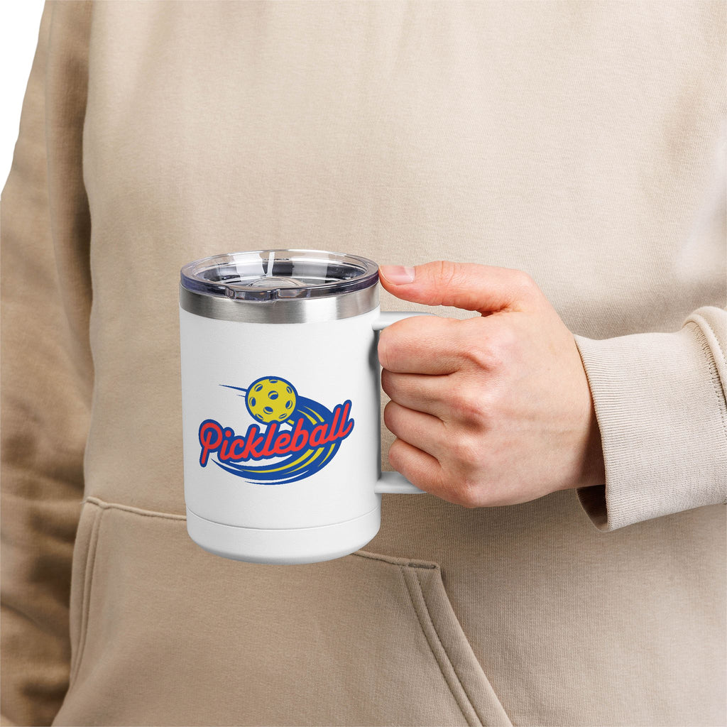 A person holding a white travel coffee mug tumbler with a lid and handle, with a classic pickleball logo featuring the word pickleball and a yellow pickleball with motion lines, against a white background
