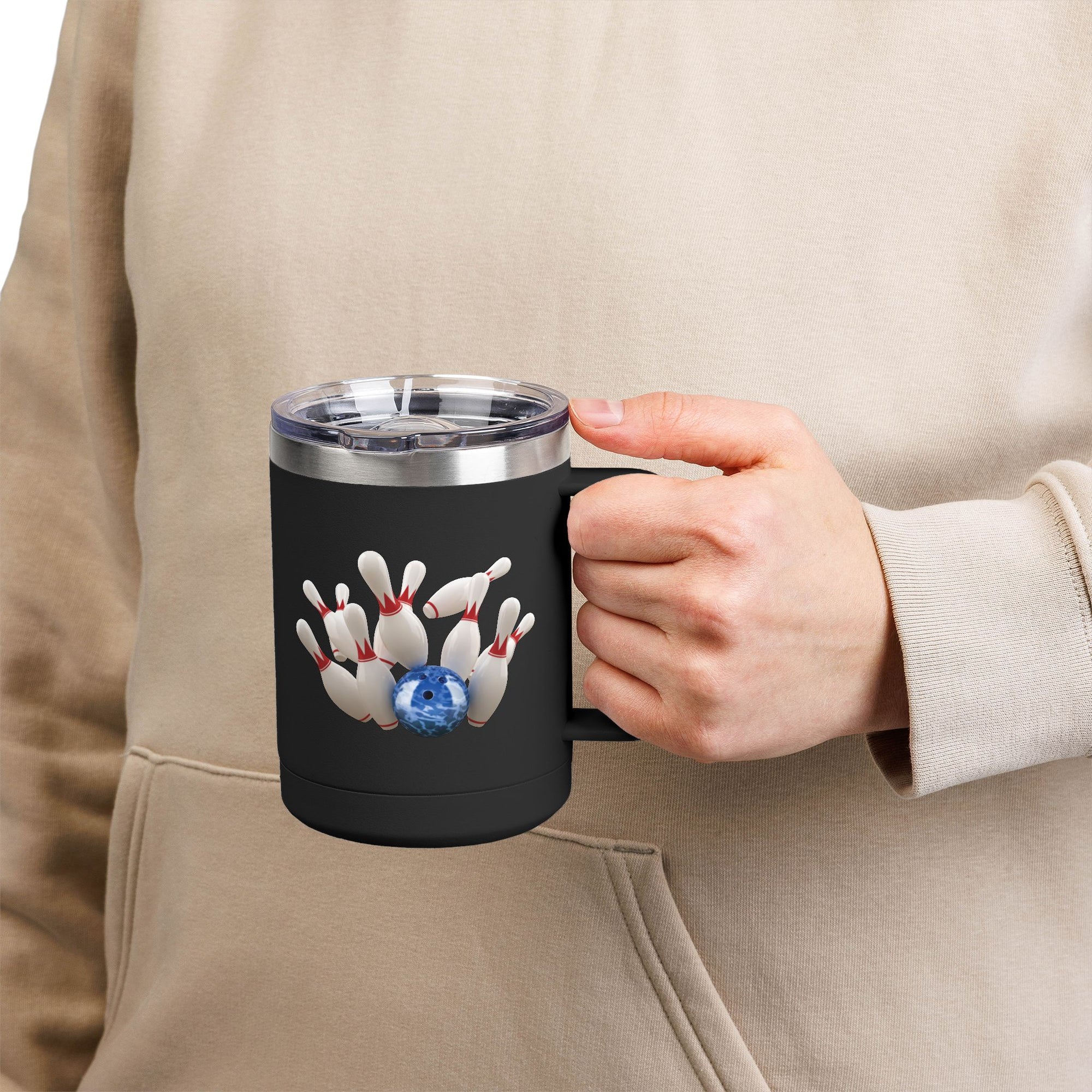 A person holding a black travel coffee tumbler mug with handle and lid, with a graphic of a blue bowling ball knocking over bowling pins