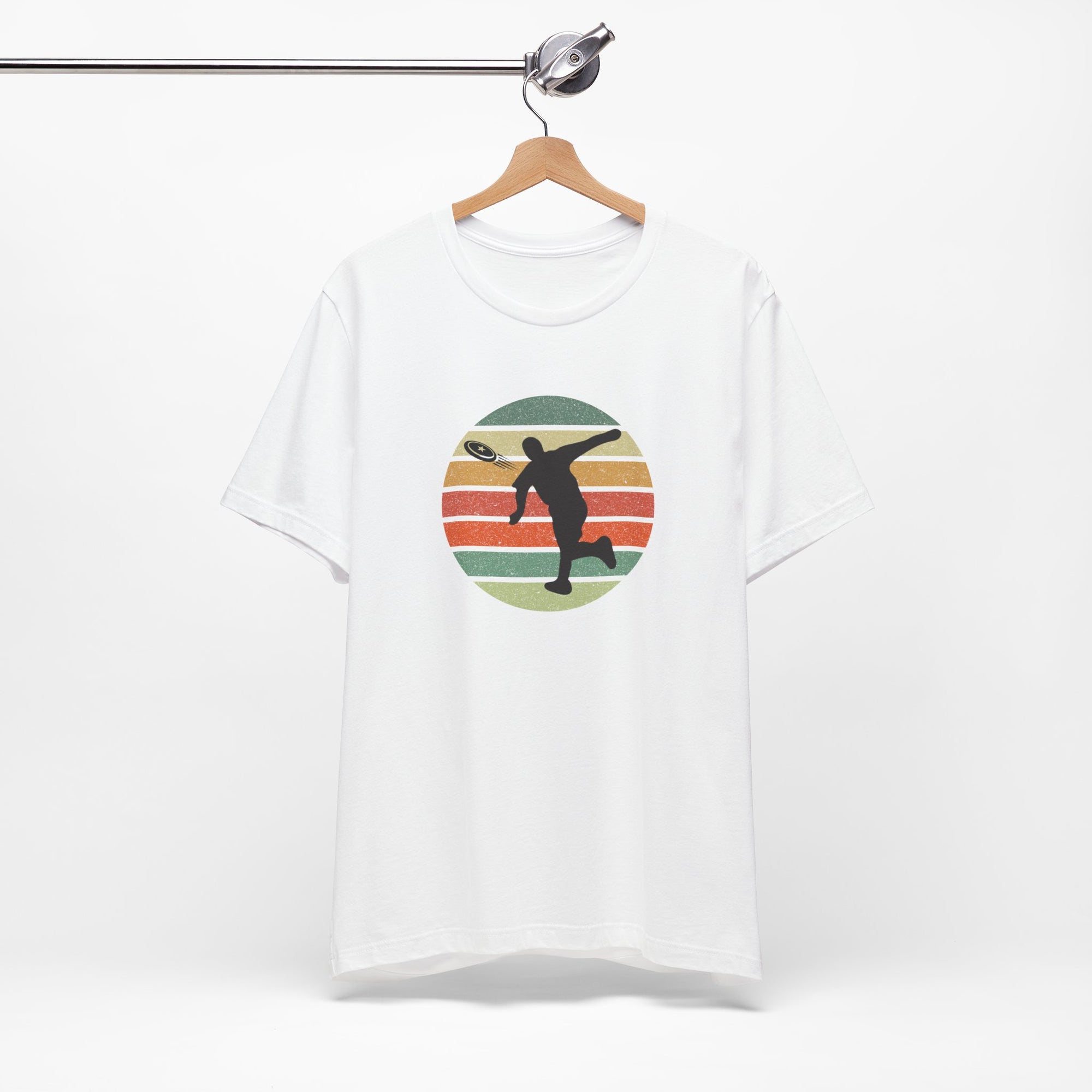White t-shirt with a graphic of a silhouette disc golf player throwing a disc above a colorful retro graphic, hanging on a wooden hanger.