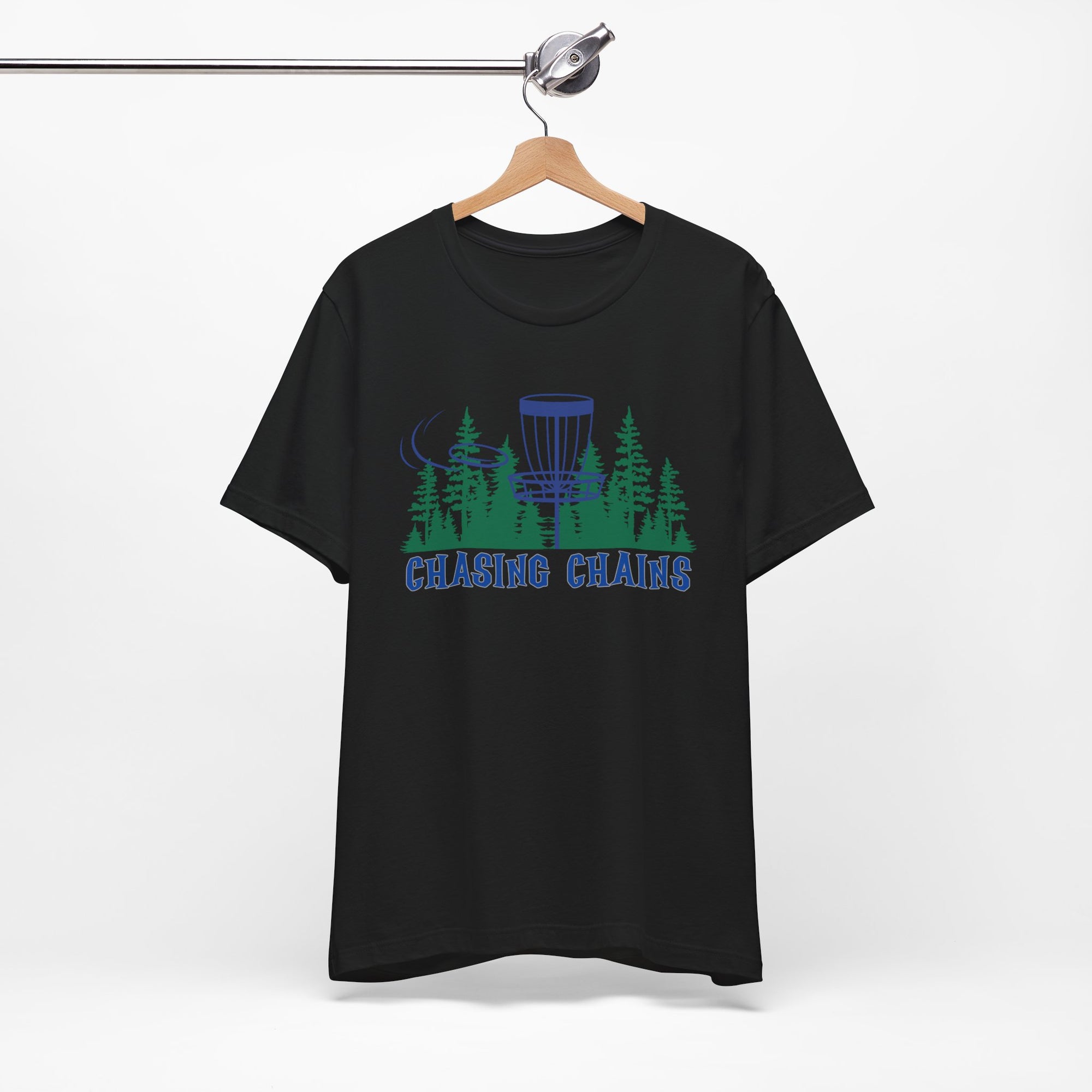 Black t-shirt with 'Chasing Chains' graphic featuring a flying disc golf disc and basket and chains in front of a scenic evergreen tree landscape, on a hanger against a white background