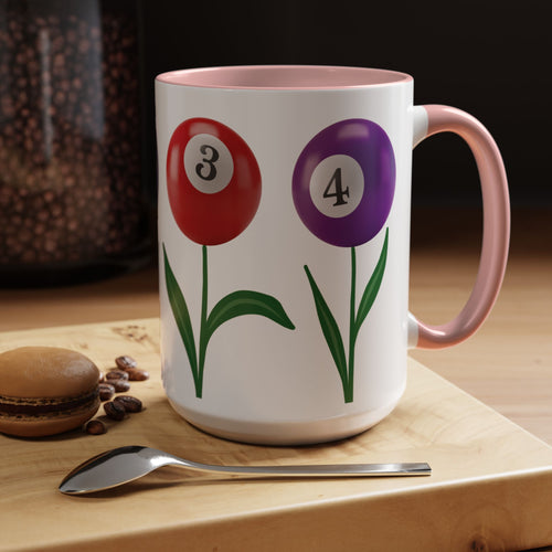 A white ceramic coffee mug with pink accents on the handle and interior, with four colorful flowers made out of billiards balls with green stems, in a coffee shop setting
